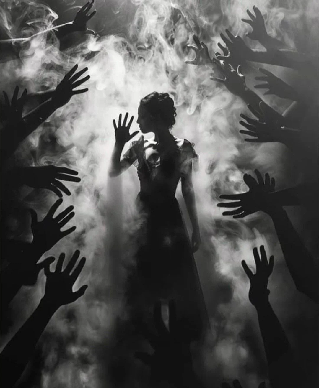 Silhouette of a woman standing amidst a foggy atmosphere with smoke, surrounded by darkened hands reaching out towards her from all sides.