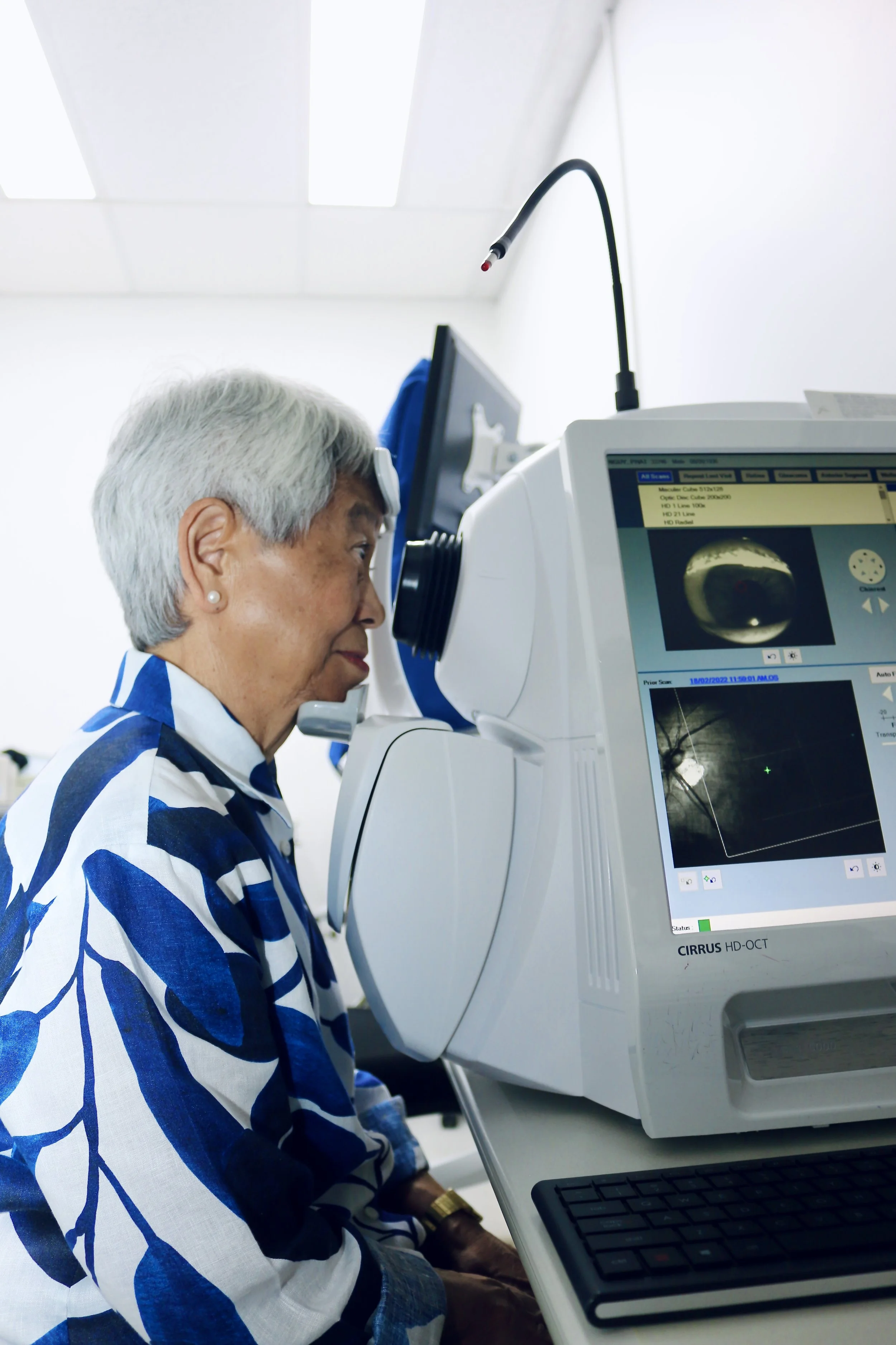 A woman with gray hair and pearl earrings uses a medical imaging machine in a clinical setting.