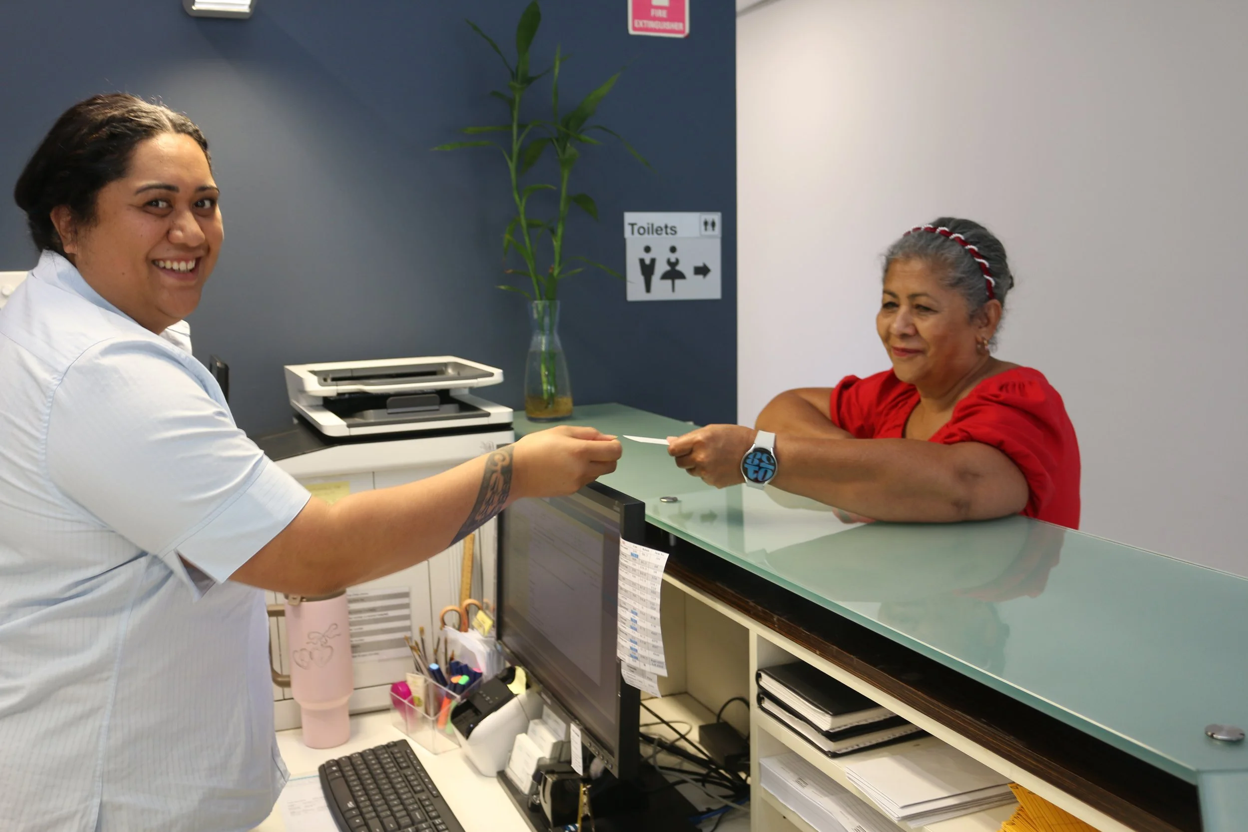 A healthcare worker verifying a patient's identification band at a reception desk in a medical office.