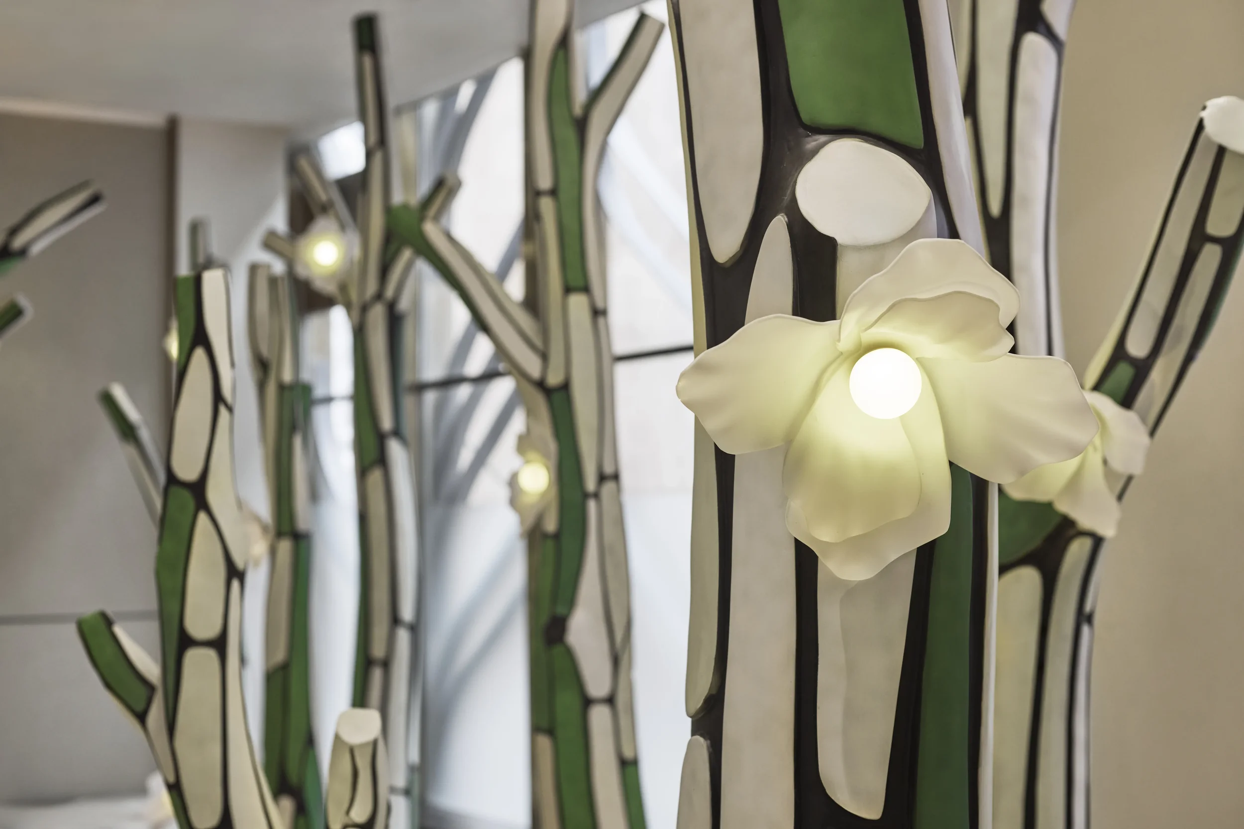 Close-up of stained glass art with green, white, and black sections, illuminated flower-shaped light fixtures at the bottom.