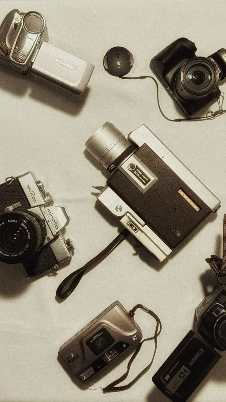 Collection of vintage cameras, a Canon digital camera, and film rolls laid out on a light-colored surface.