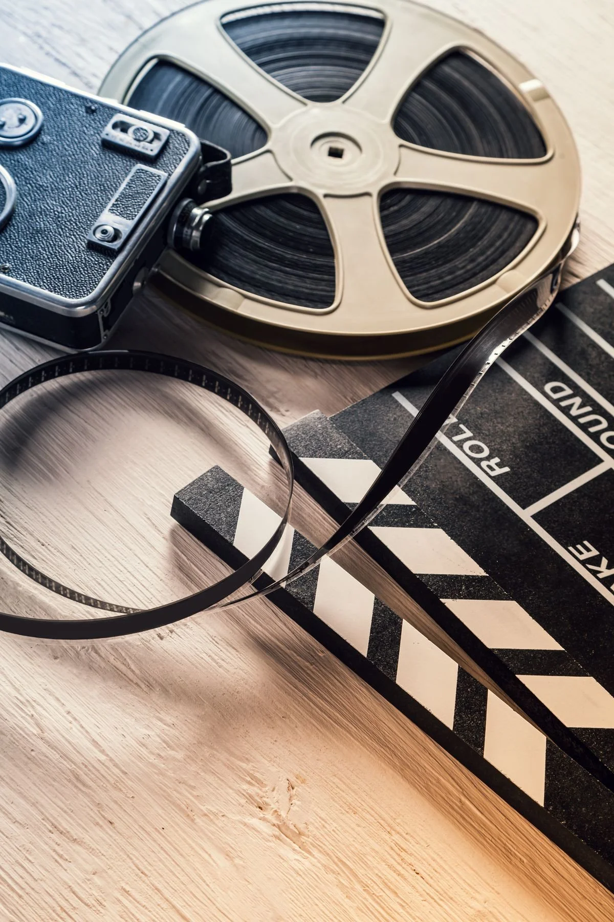 A film reel, a vintage camera, a clapperboard, and a film strip on a wooden surface.