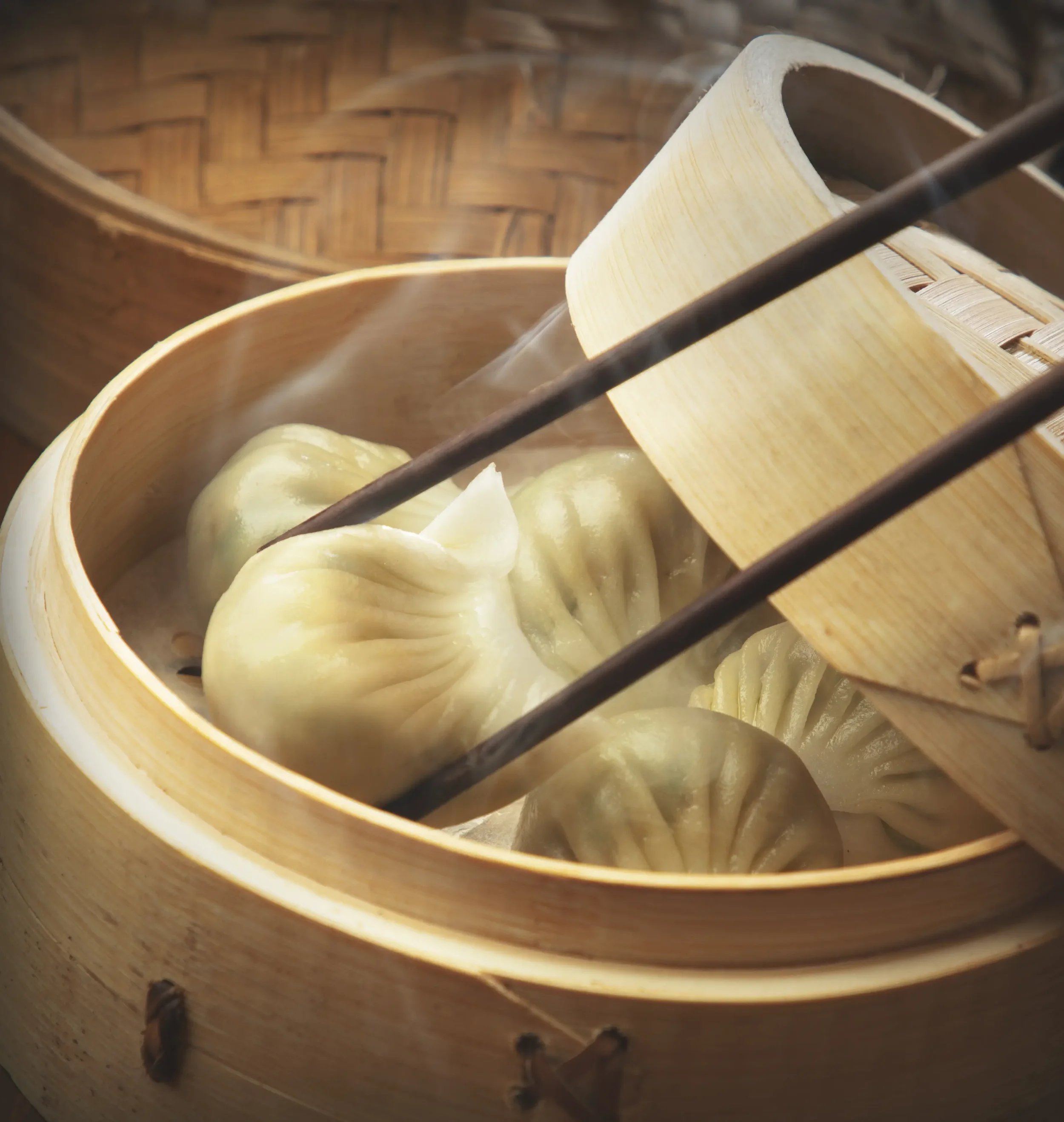 Steaming dumplings in a bamboo steamer with chopsticks.