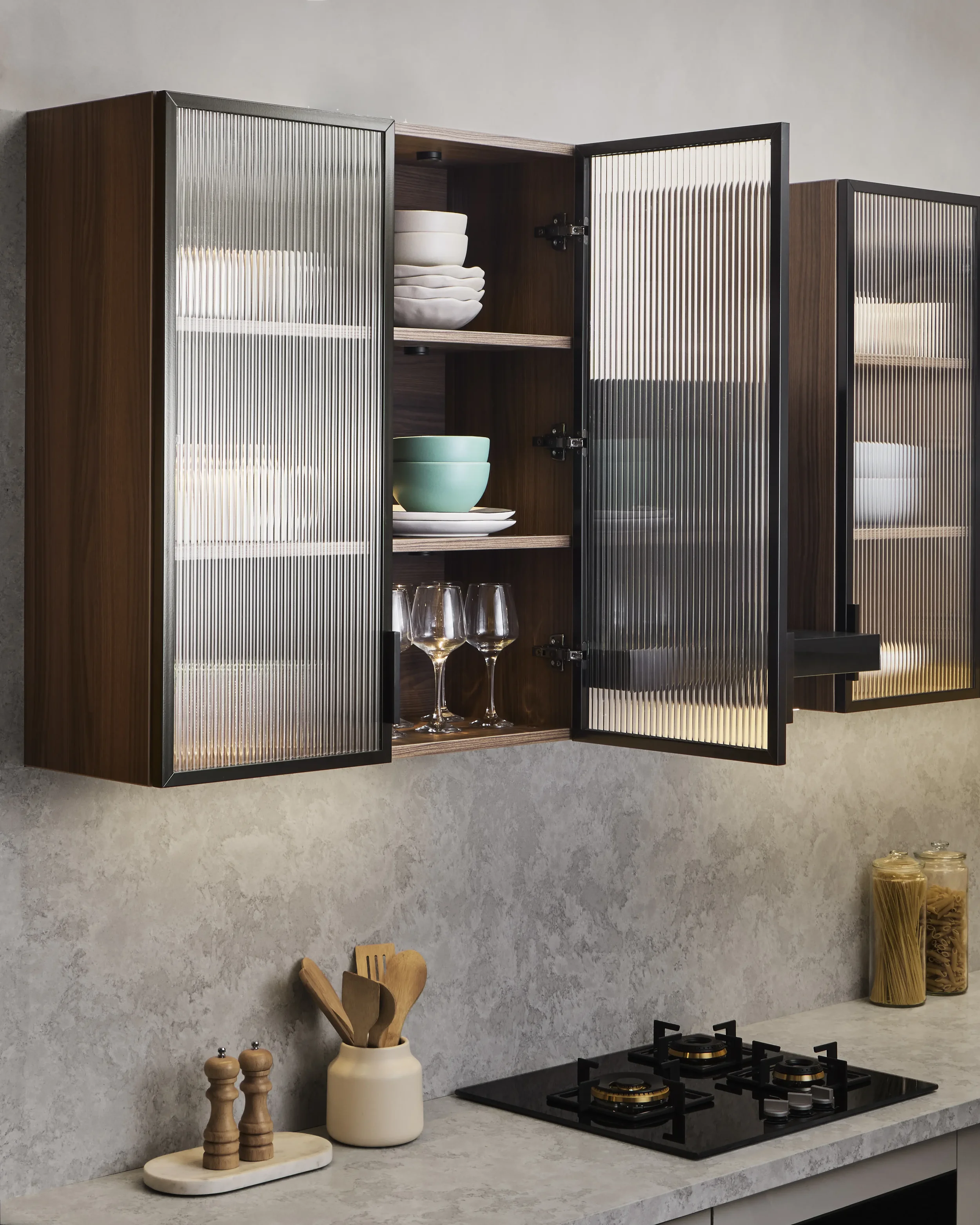 Modern kitchen with beige marble countertop, gray textured backsplash, wall-mounted cabinet with wood and metal design, countertop appliances, and kitchen utensils.