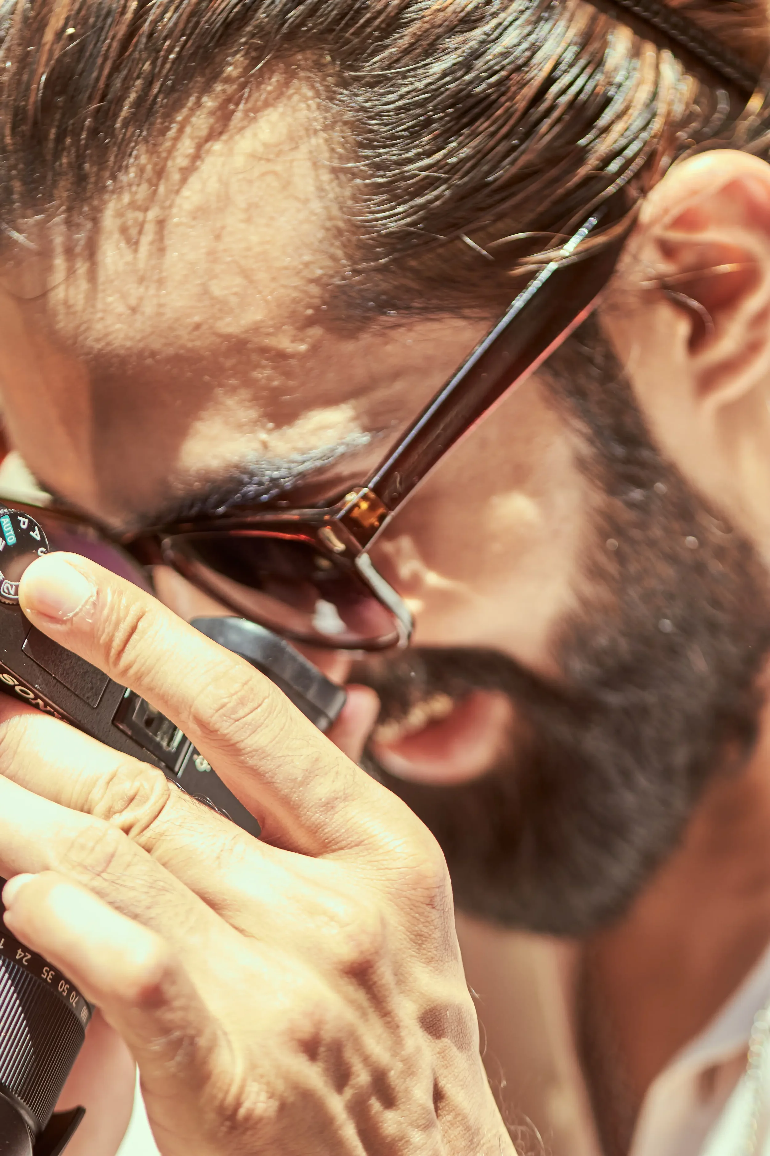 A man with glasses and a beard looking through a camera viewfinder, pressing the shutter button.