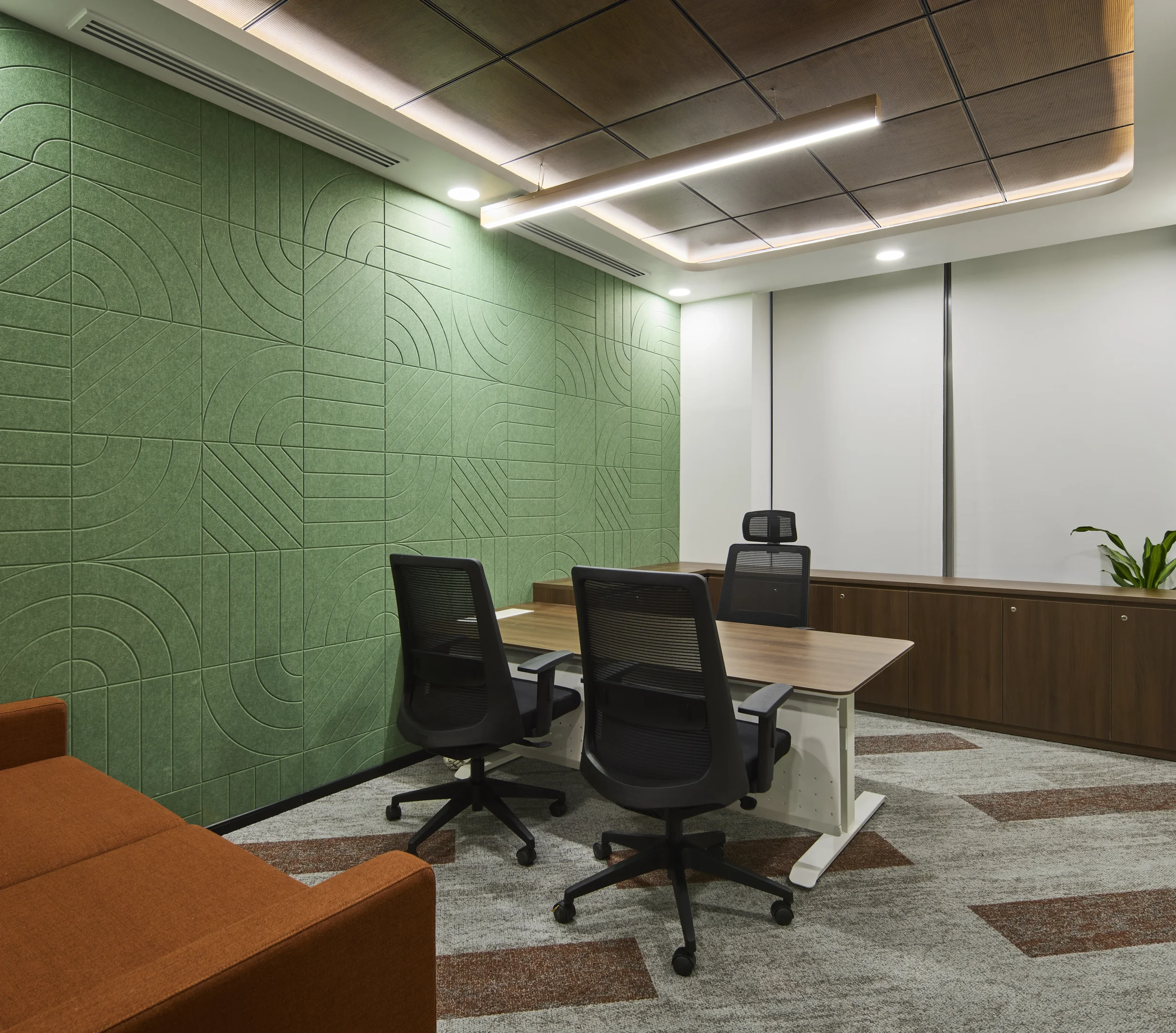 Modern office conference room with a wooden table, black chairs, green textured wall, white wall, and brown ceiling with built-in lighting.