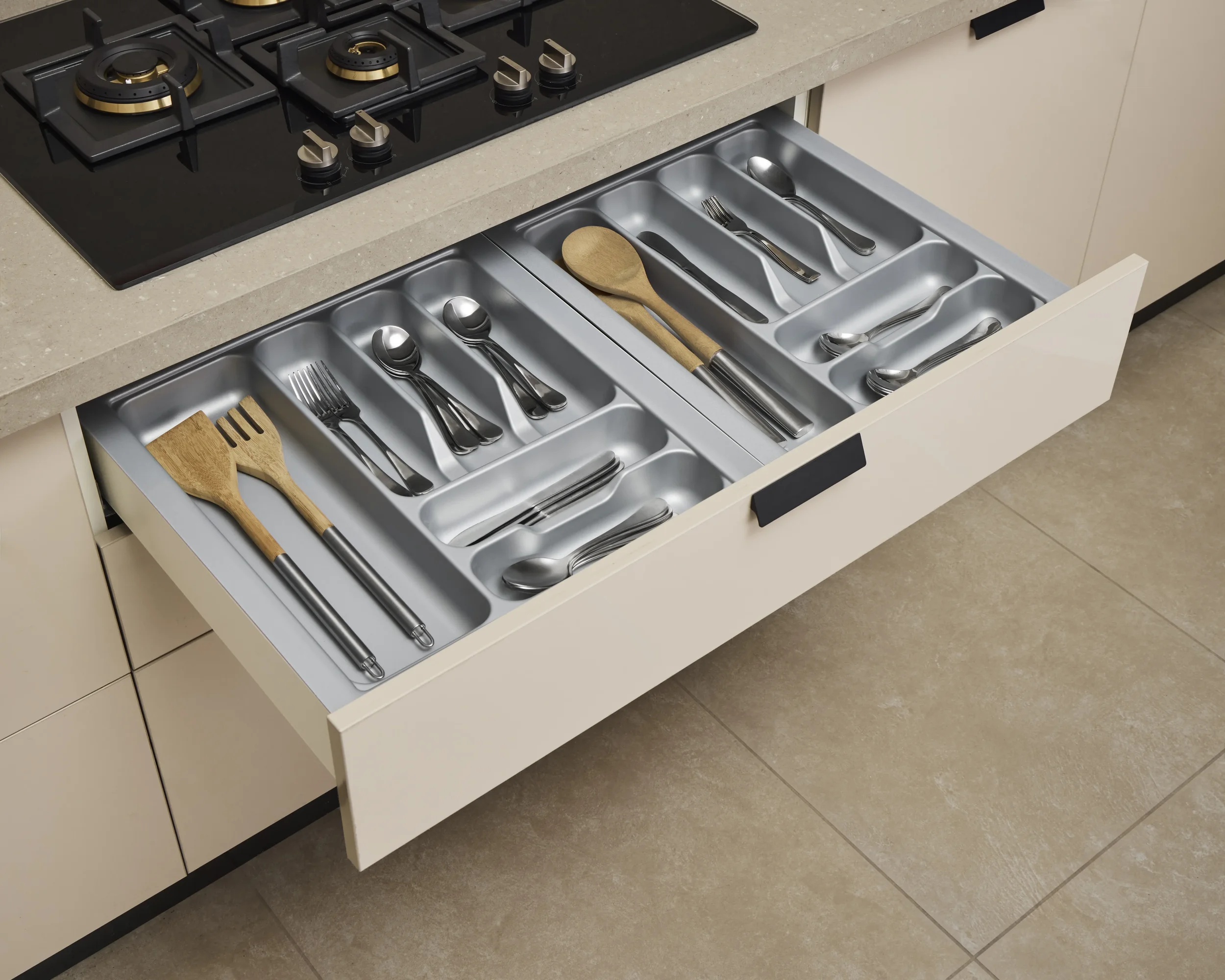 Kitchen drawer open to reveal utensils including knives, forks, spoons, and wooden spatulas, with a countertop and stove above.