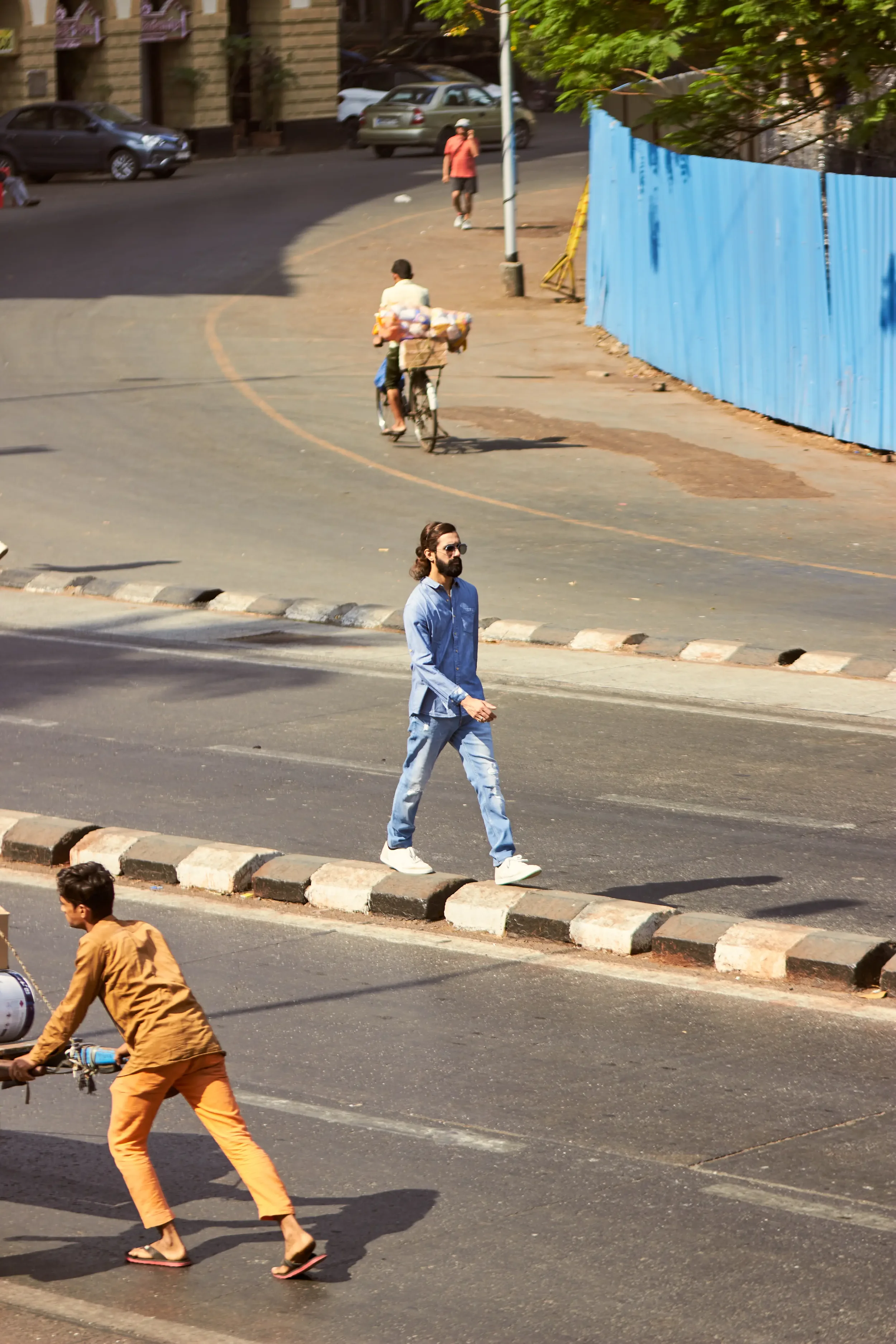 People walking and cycling on a city street with traffic and parked cars in the background.
