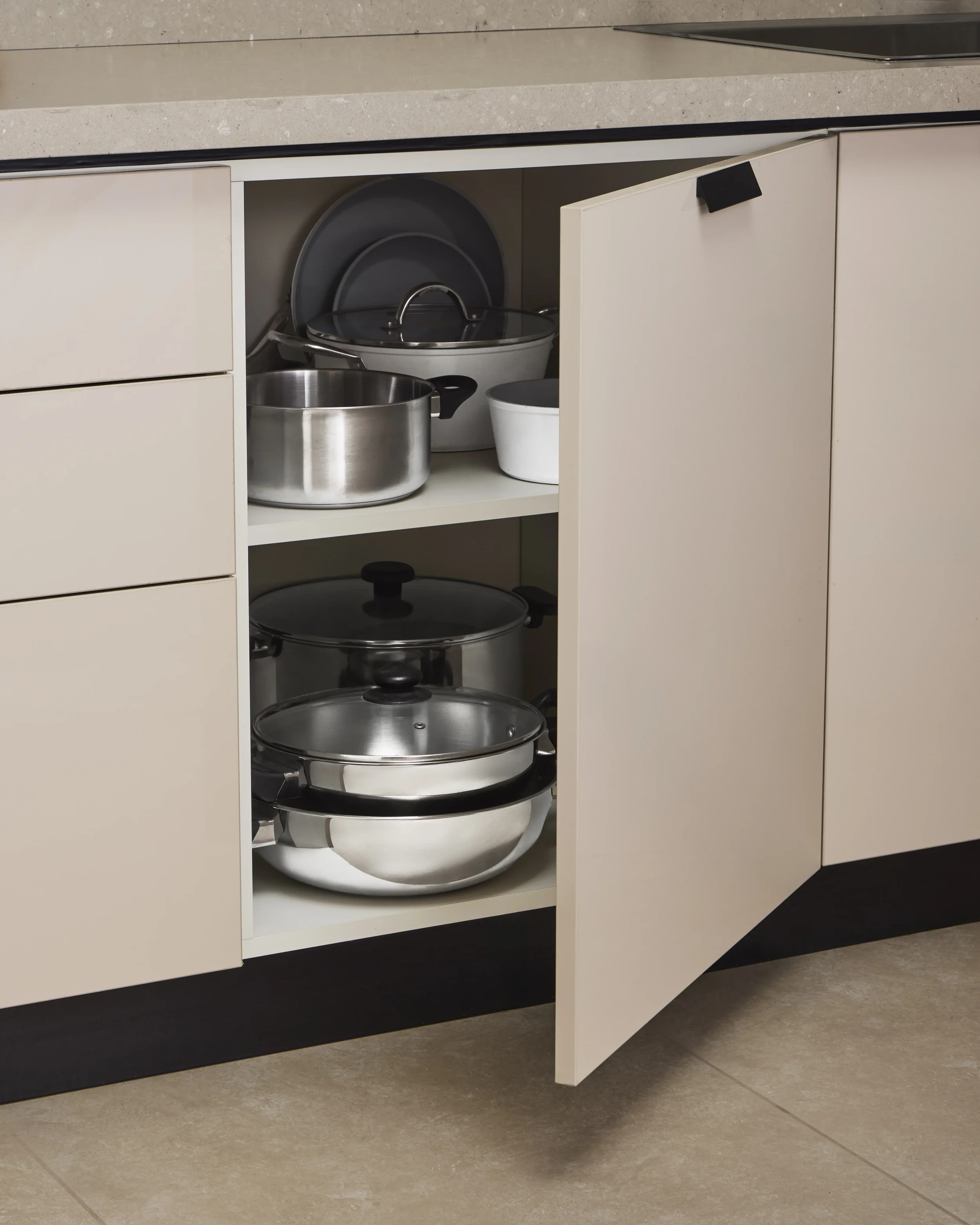Open kitchen cabinet with various pots and bowls inside, located beneath a beige countertop.