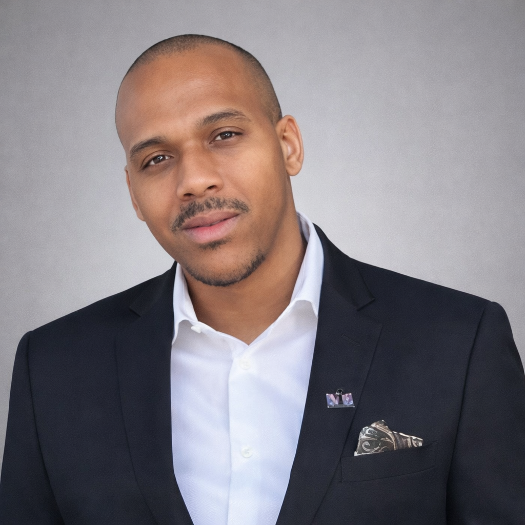 A man in a dark suit and white shirt looking at the camera with a neutral expression.