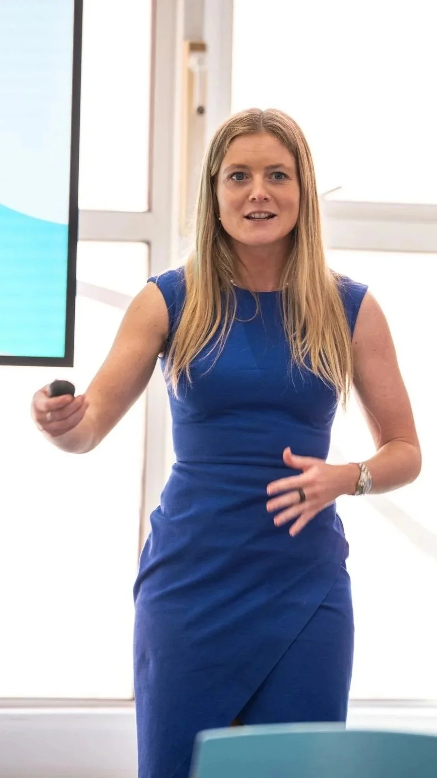 Woman in a blue dress presenting with a remote in front of a screen