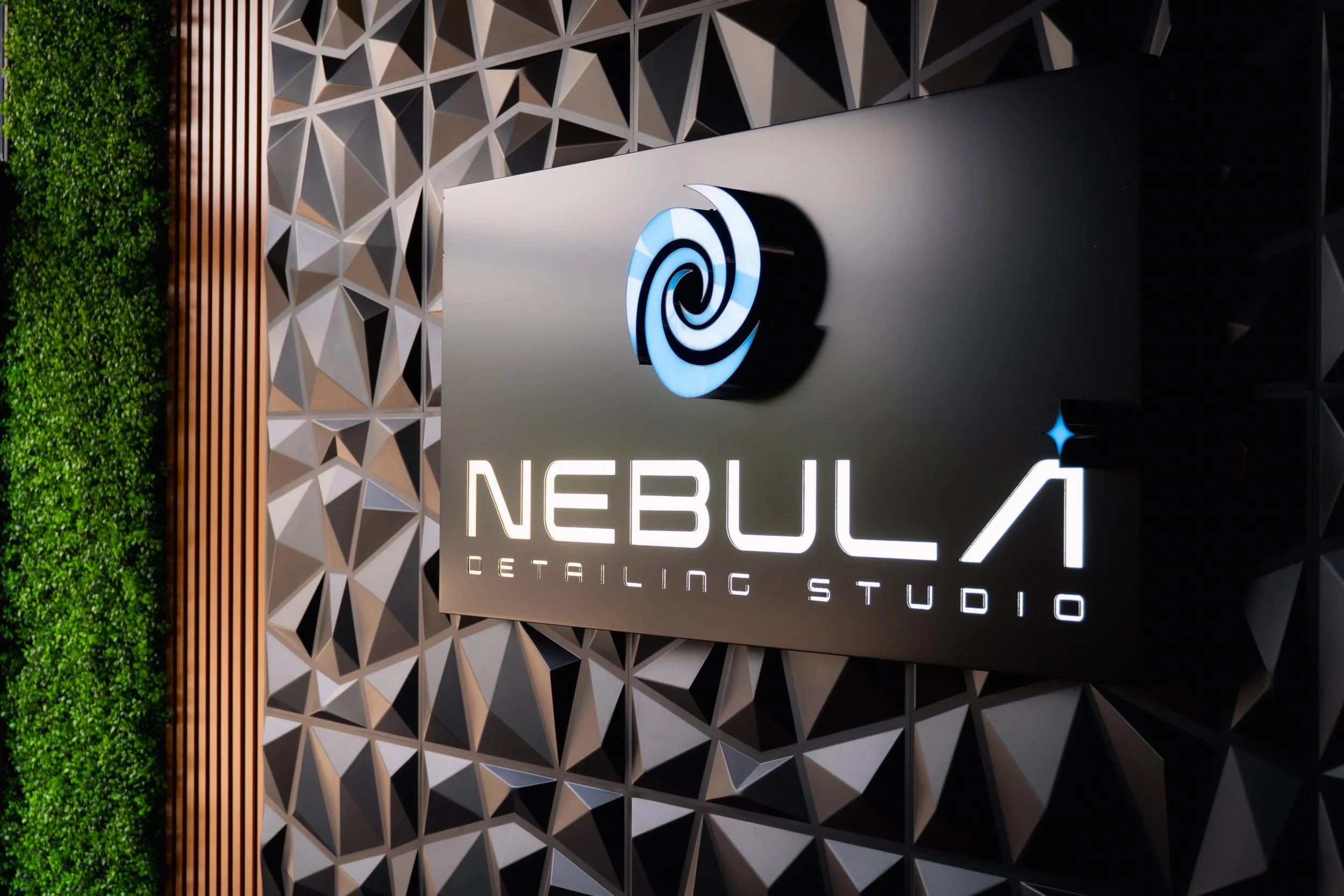 A modern wall with geometric 3D tile pattern, green wall on the left, and a logo for Nebula Detailing Studio illuminated on a black background.