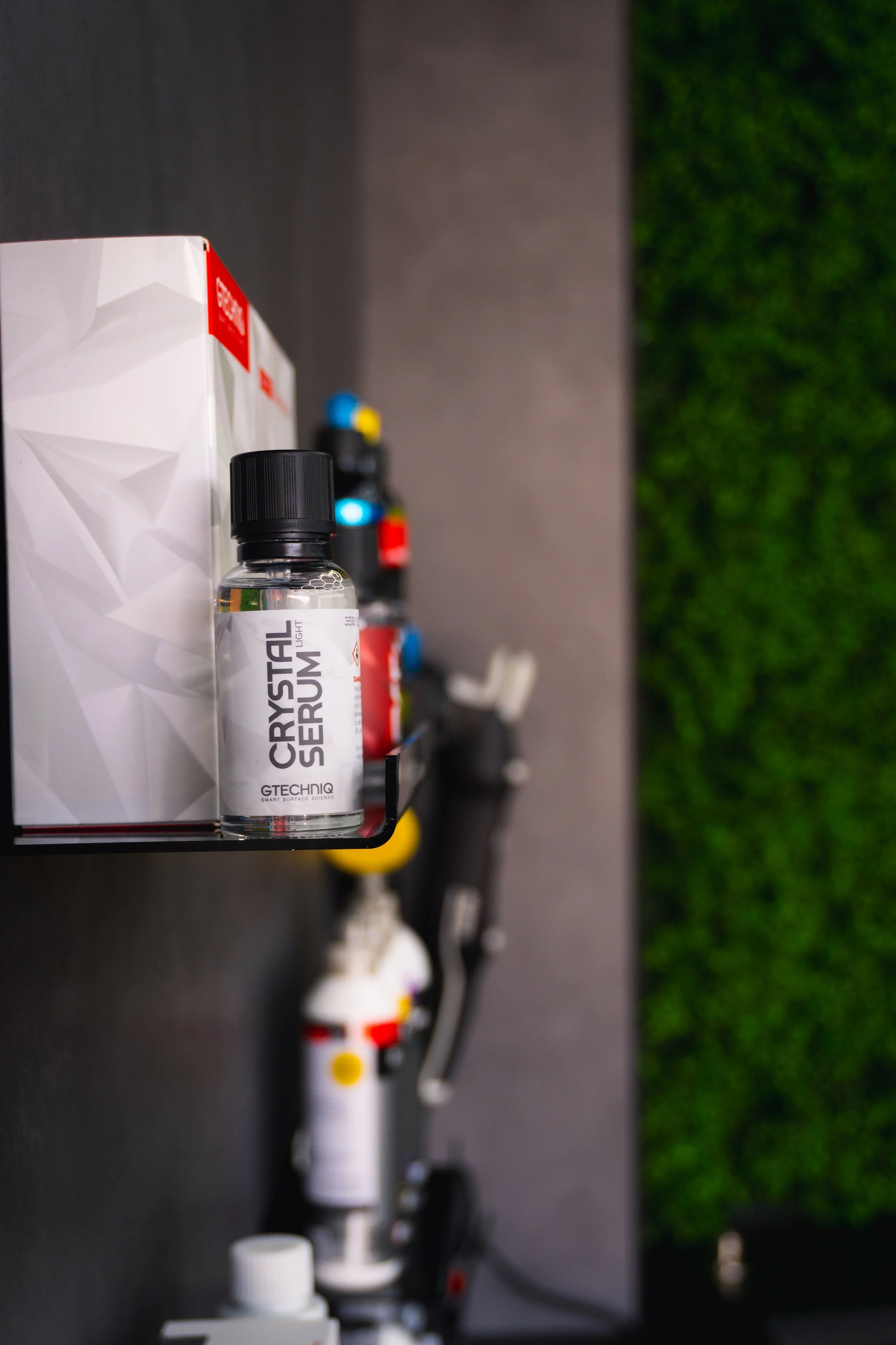 Close-up of a small bottle labeled 'CRYSTAL SERUM' on a black surface, with cleaning supplies and a green wall in the background.