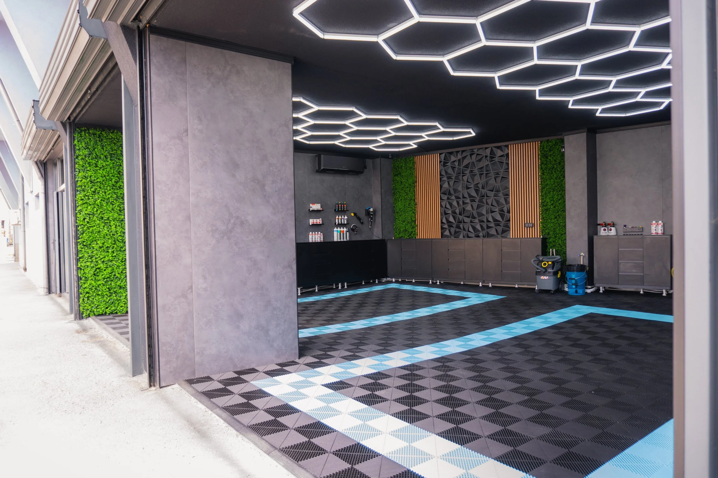 Modern car wash with geometric lighting on the ceiling, green plants on the walls, and a black and blueCheckered floor.