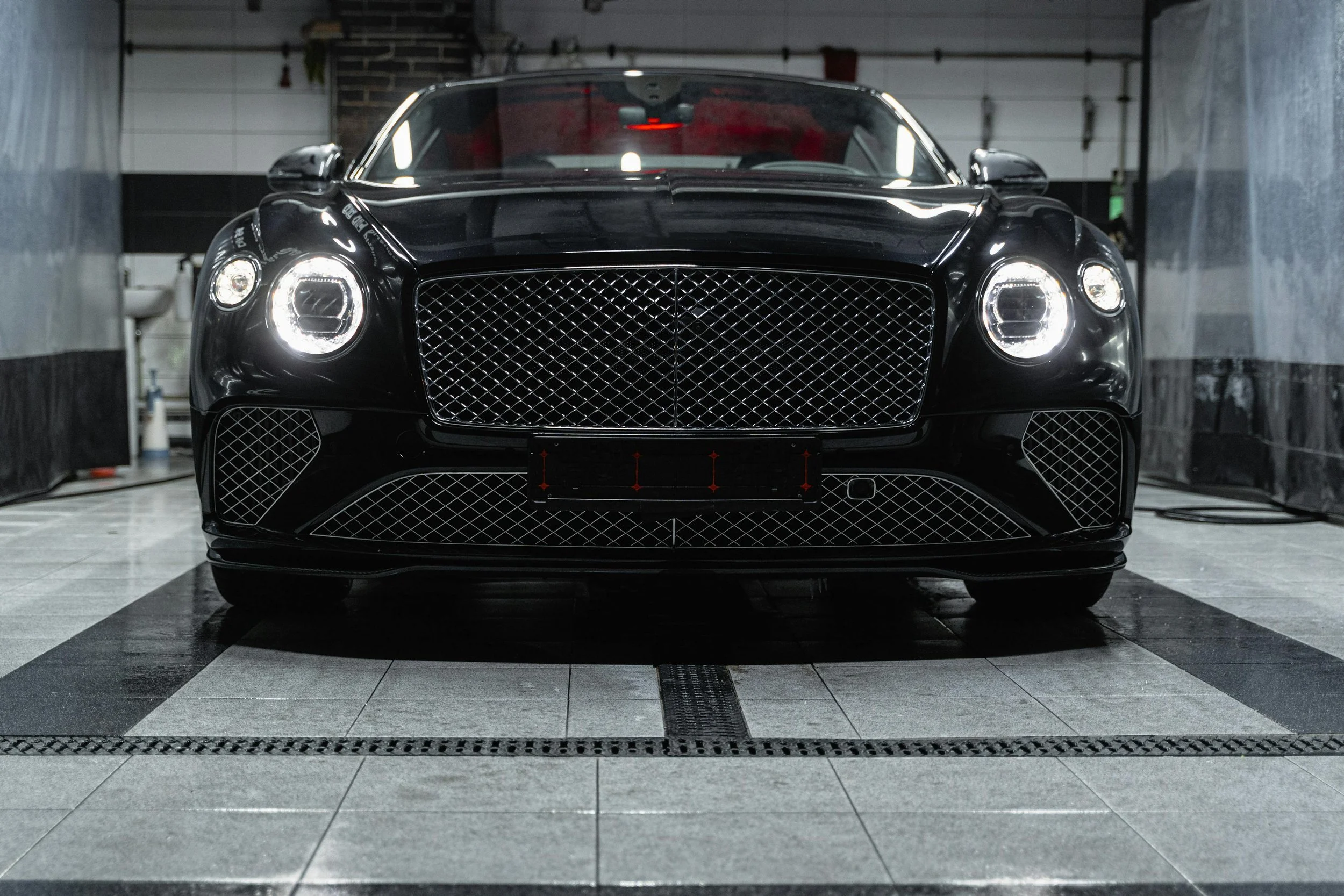 Black luxury sports car parked inside an industrial garage with tiled flooring and metal walls.