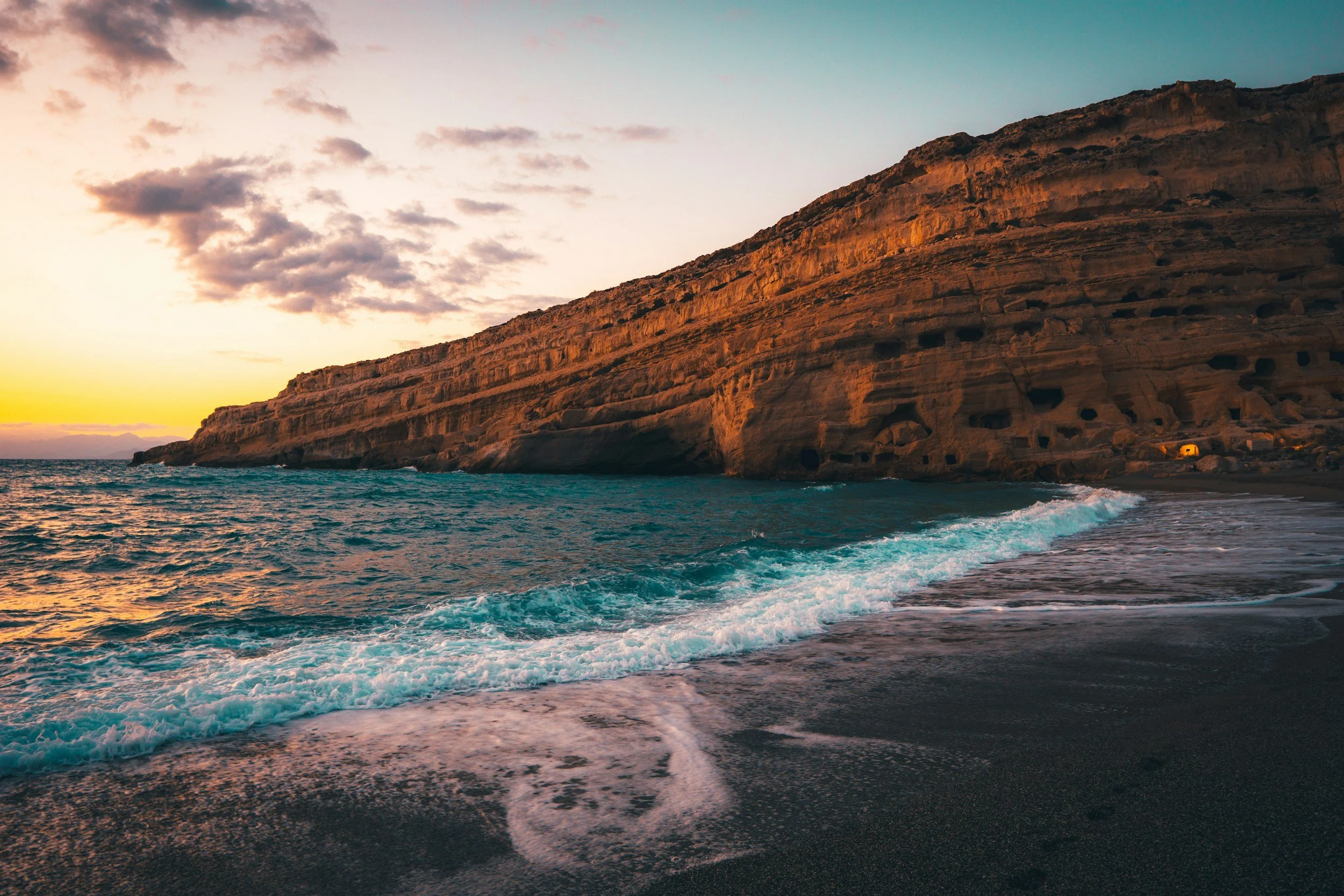 Matala Beach in South Crete at sunset with cliffside tombs.