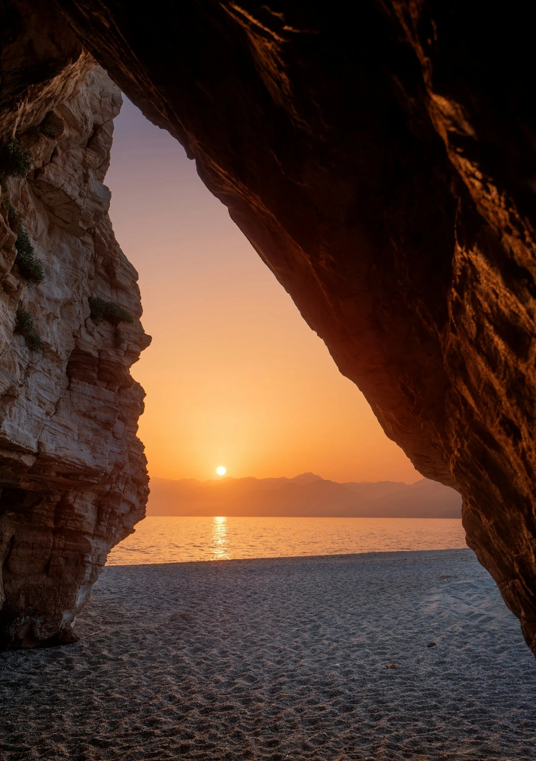 Rocks frame a sunset behind a beach in Crete.