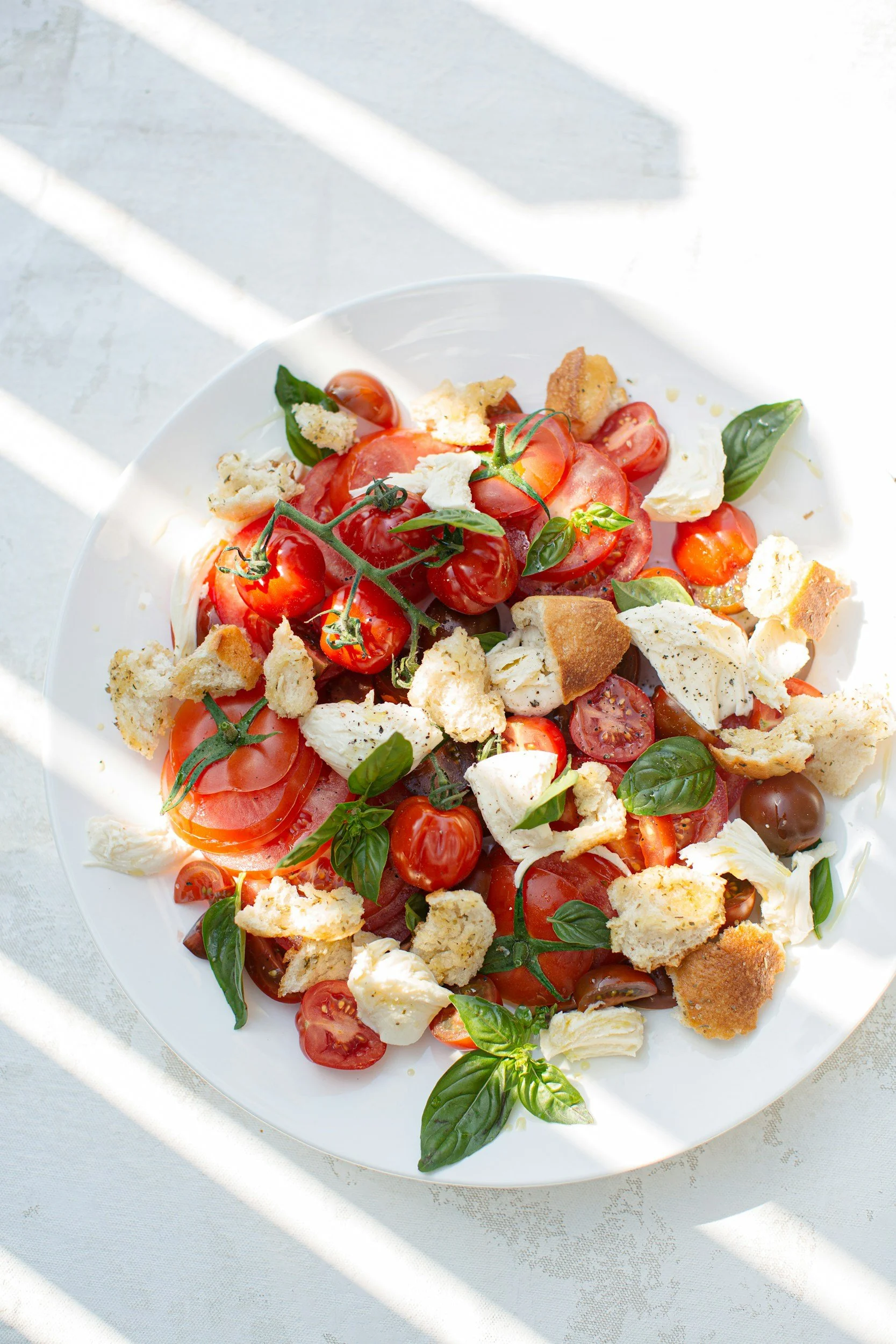 Photo of a Cretan salad with tomatoes, feta cheese and hard bread on a white table top.