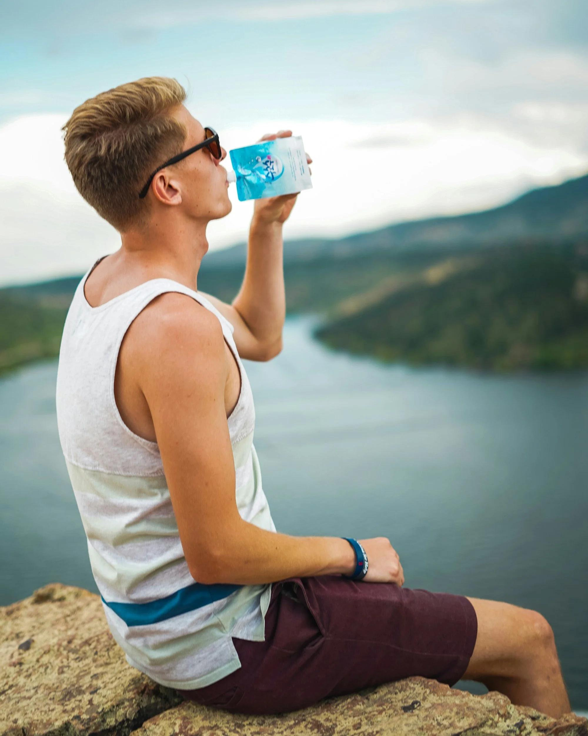 Man sitting on a stone overlooking a lake and drinking water after hiking in South Crete