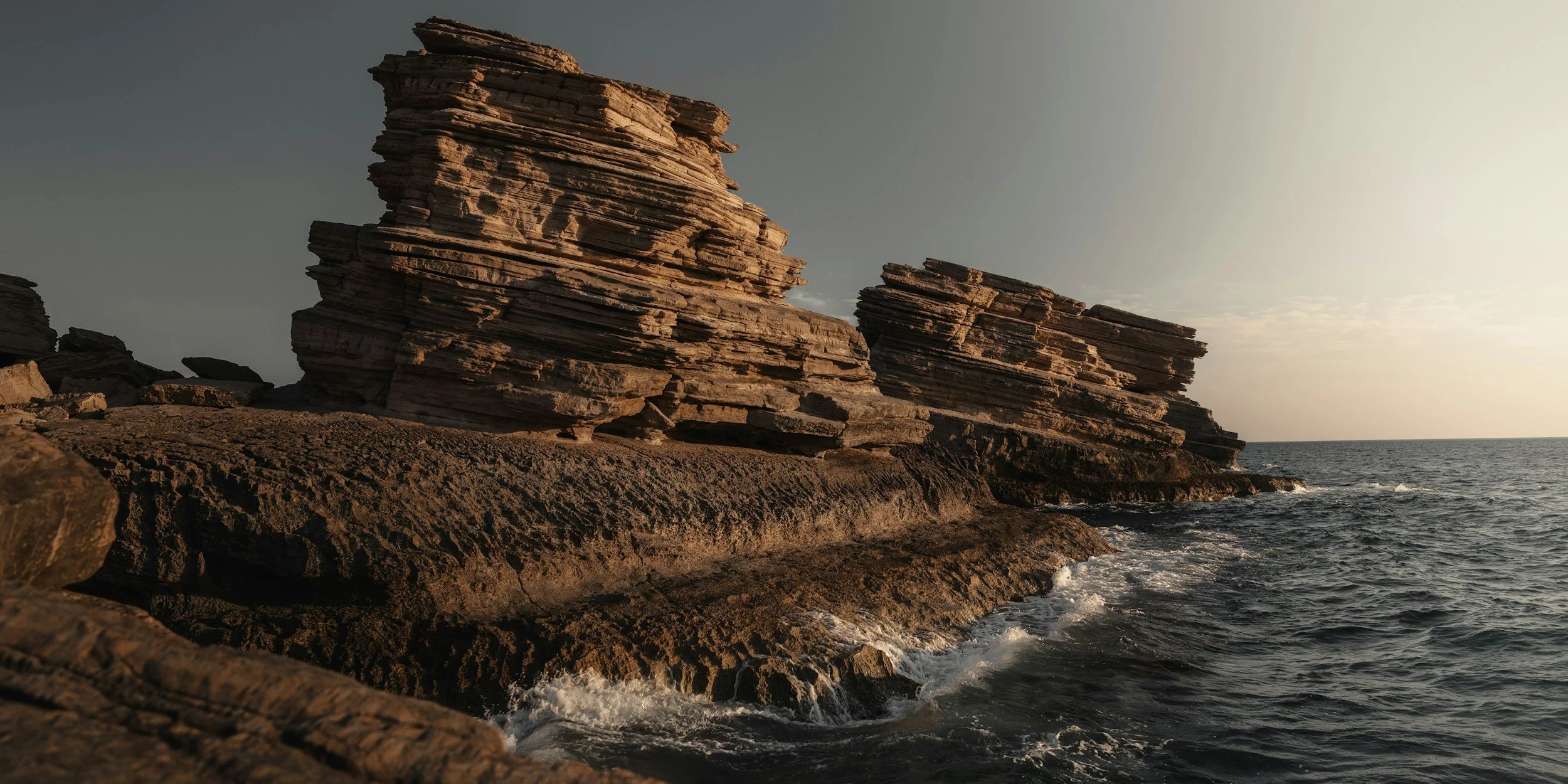 Layered sandstone formations at Triopetra Beach meet the Libyan Sea in the evening light.
