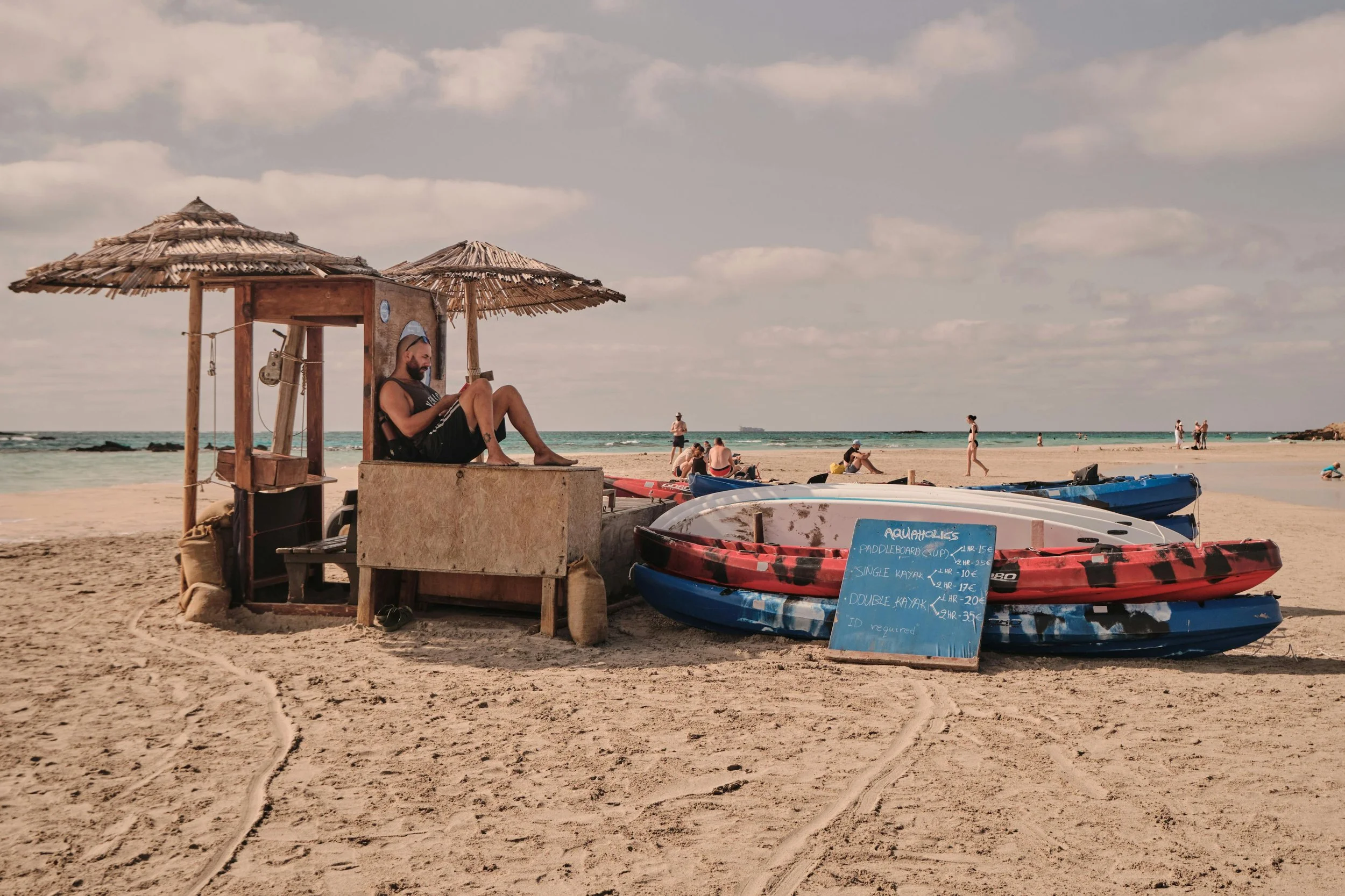 Man sitting under an umbrella on a beach in South Crete next to kayaks.