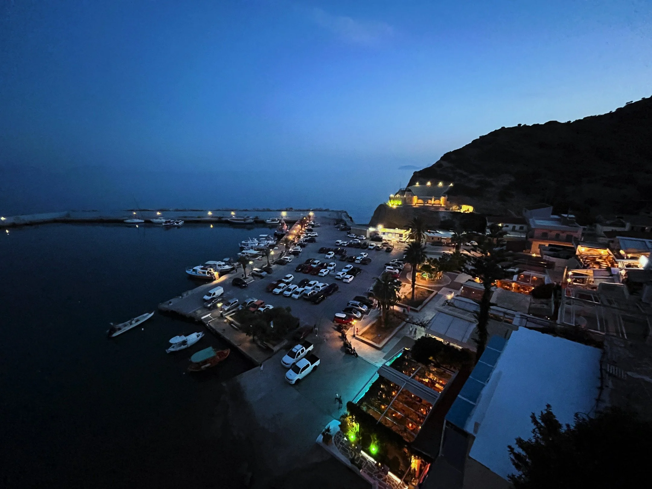 Evening view of Agia Galini harbour illuminated at dusk, with fishing boats, waterfront restaurants and the sheltered bay on Crete's south coast.