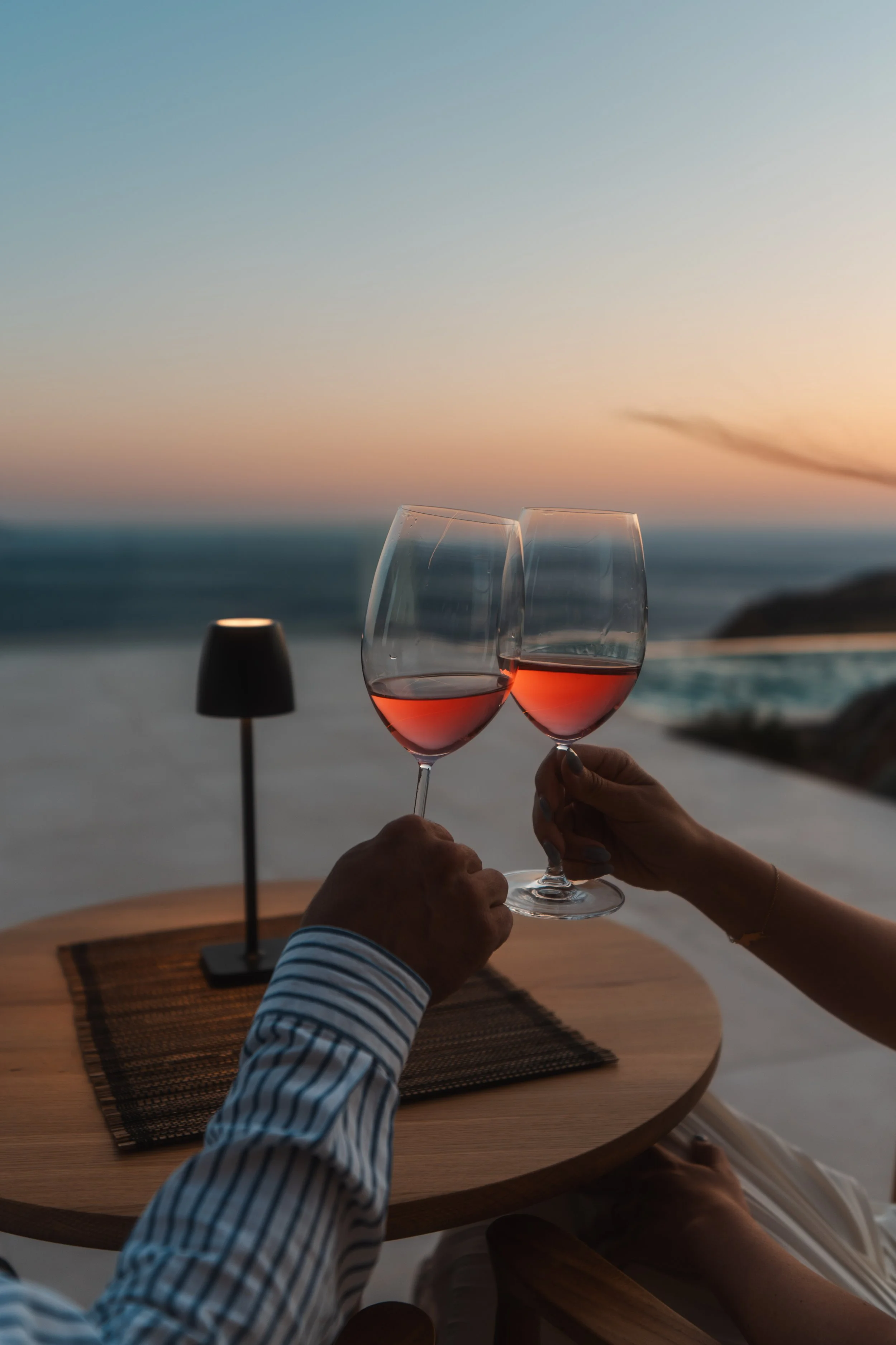 A closeup of a man and a woman toasting with wine during sunset at luxury villa in Crete.