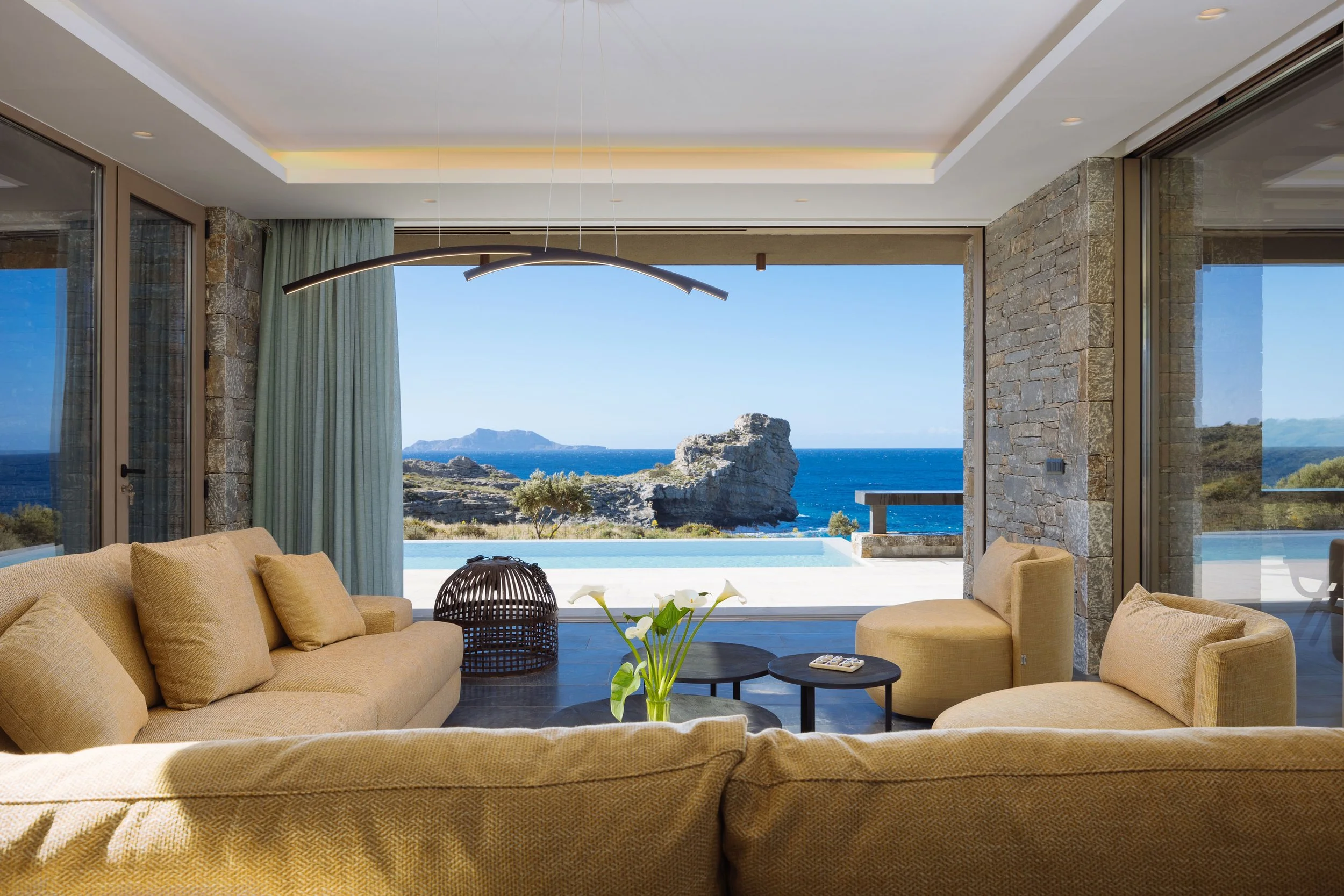 Modern living space of SeaCrete villa in Agios Pavlos with seamless indoor-outdoor design, opening onto an infinity pool and panoramic sea views of Aniforas Bay