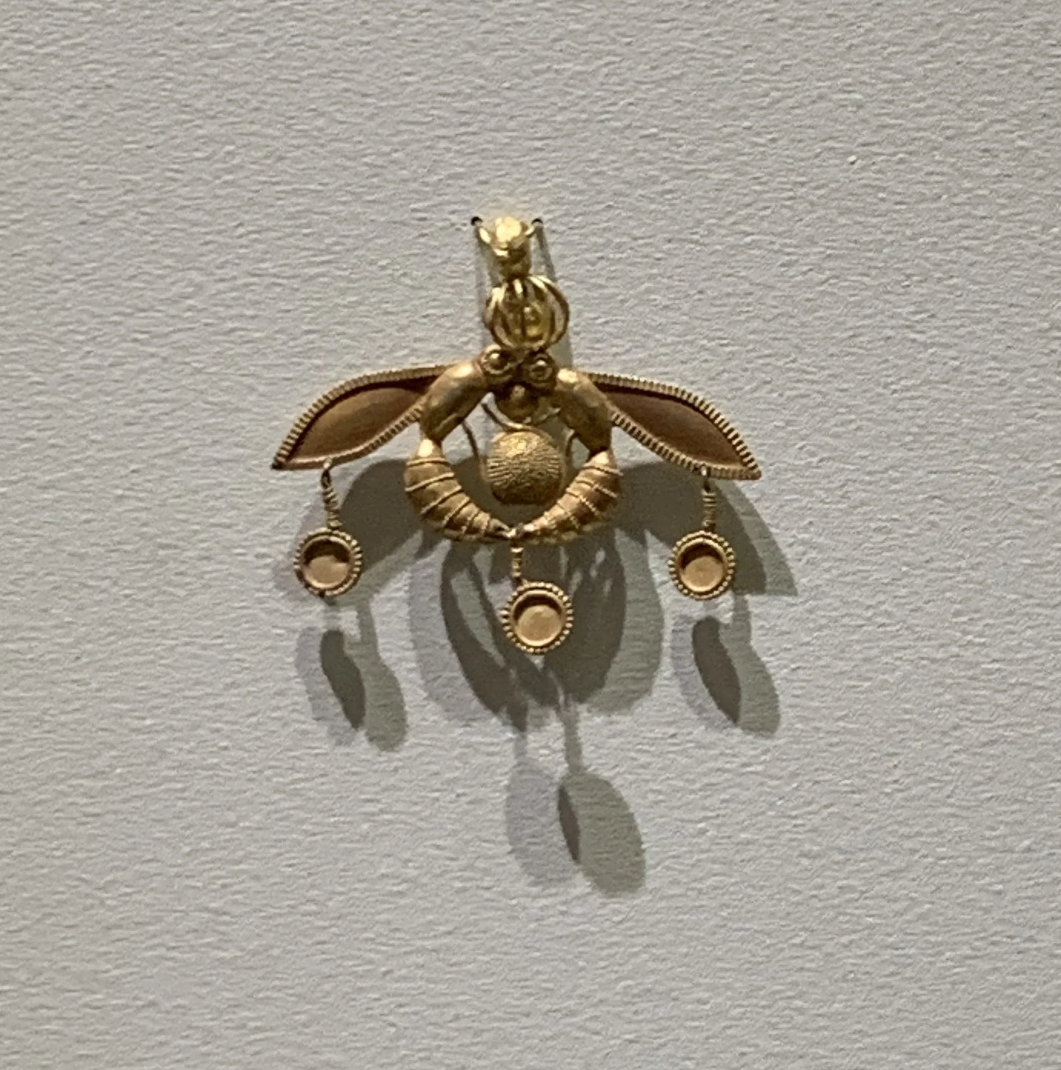 The Malia Bee Pendant, an intricate gold Minoan jewel depicting two bees around a honeycomb, displayed in the Archaeological Museum of Heraklion.
