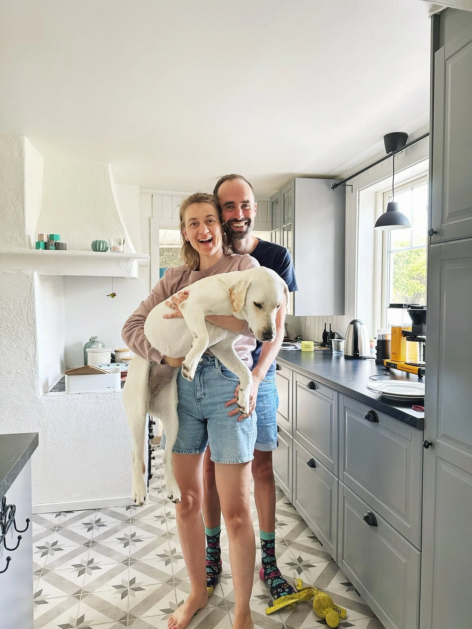 Ein fröhliches Paar hält ein Welpe in der Küche, lachend und posierend.