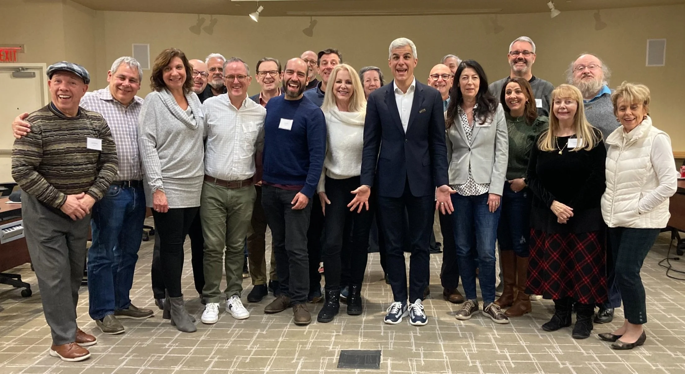 Group of diverse adults standing indoors, smiling, posing for a photo at a professional or social event.