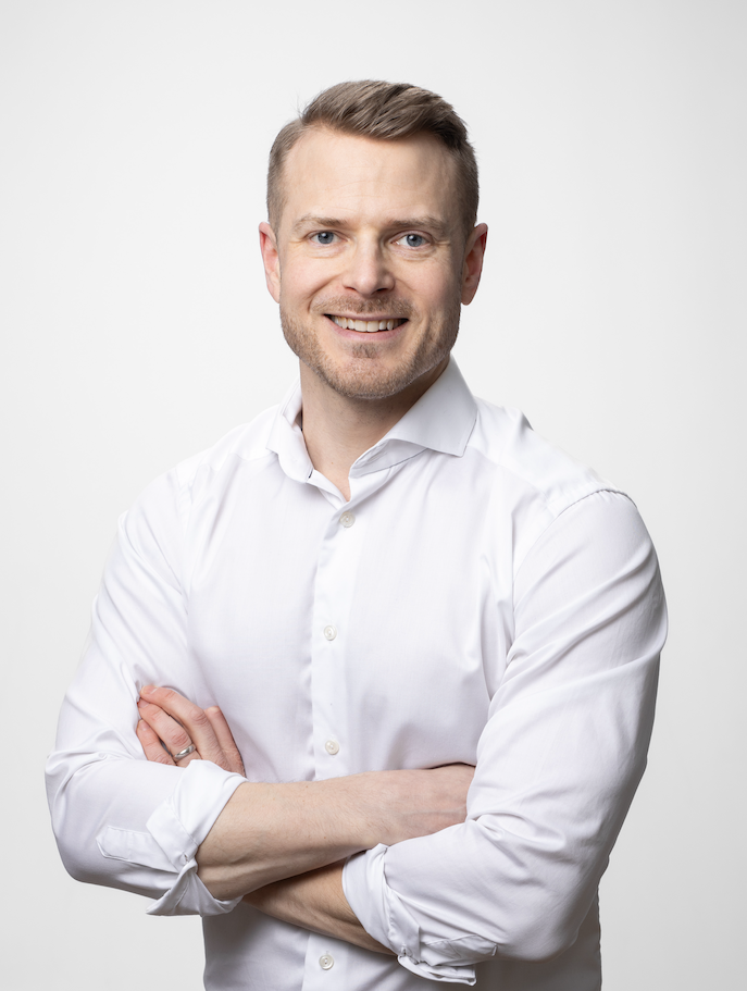 En man i vit skjorta som står med armar korsade framför en vit bakgrund.