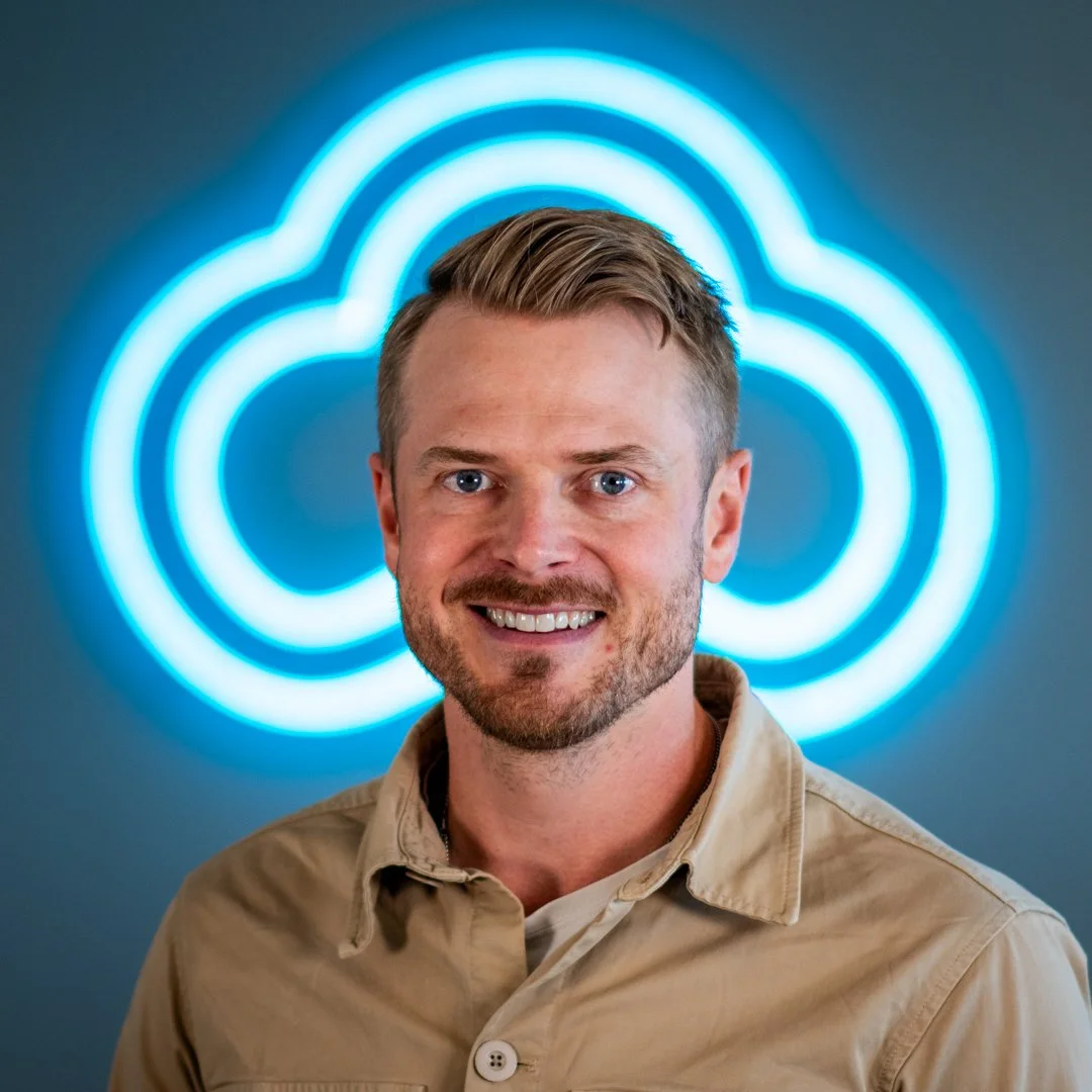 Smiling man with short hair and beard in front of a neon blue cloud logo.