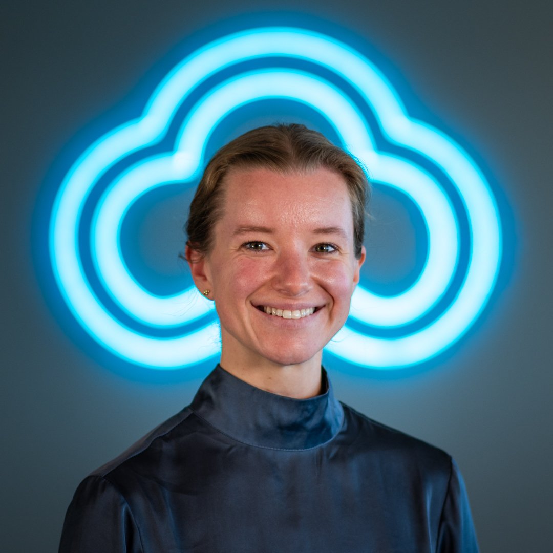 A woman with short hair smiling in front of a illuminated blue cloud icon sign.