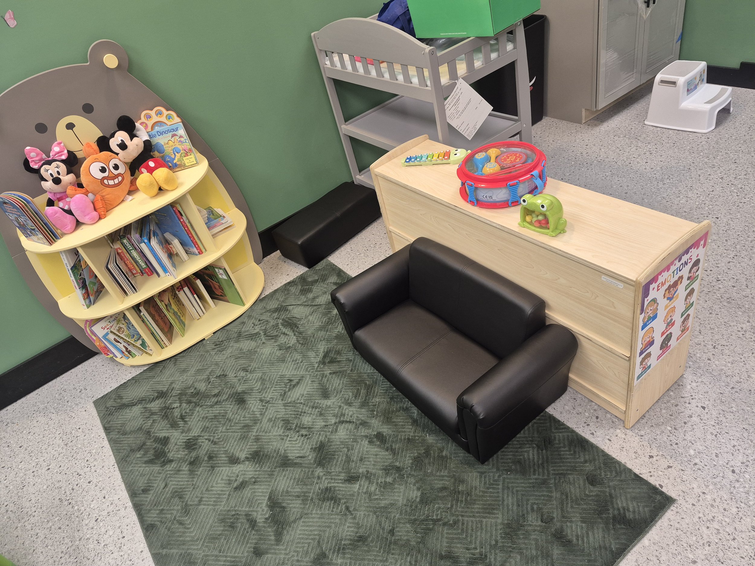 Low book display and child-sized sofa beside classroom activity shelves.