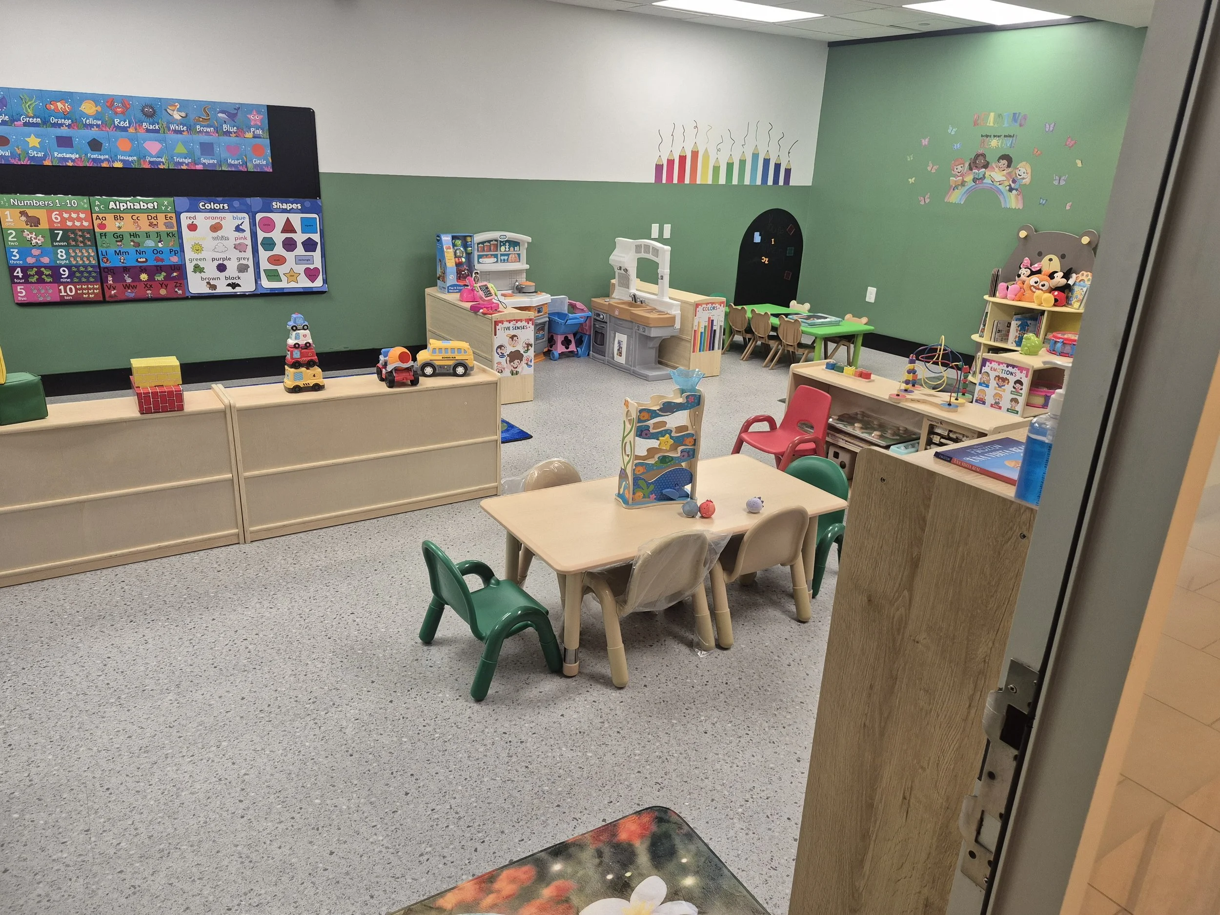 Green classroom with child-sized tables, activity materials, and low shelves.