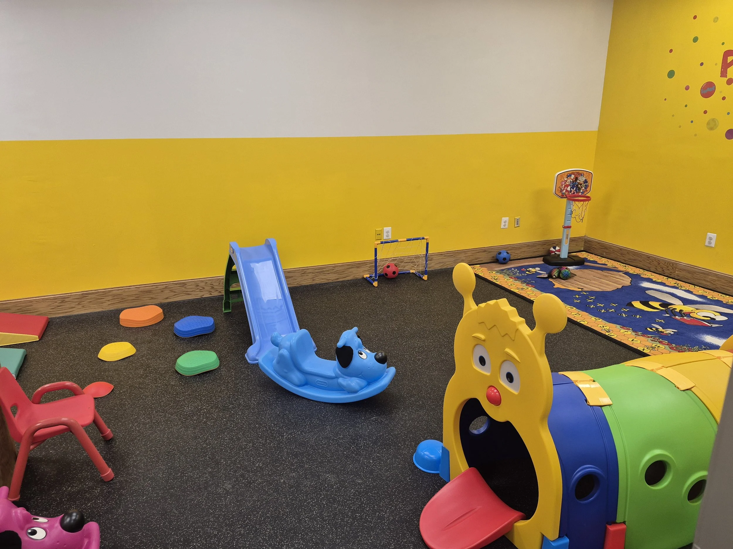 Colorful play tunnel, small slide, and rocking toys in the indoor playroom.