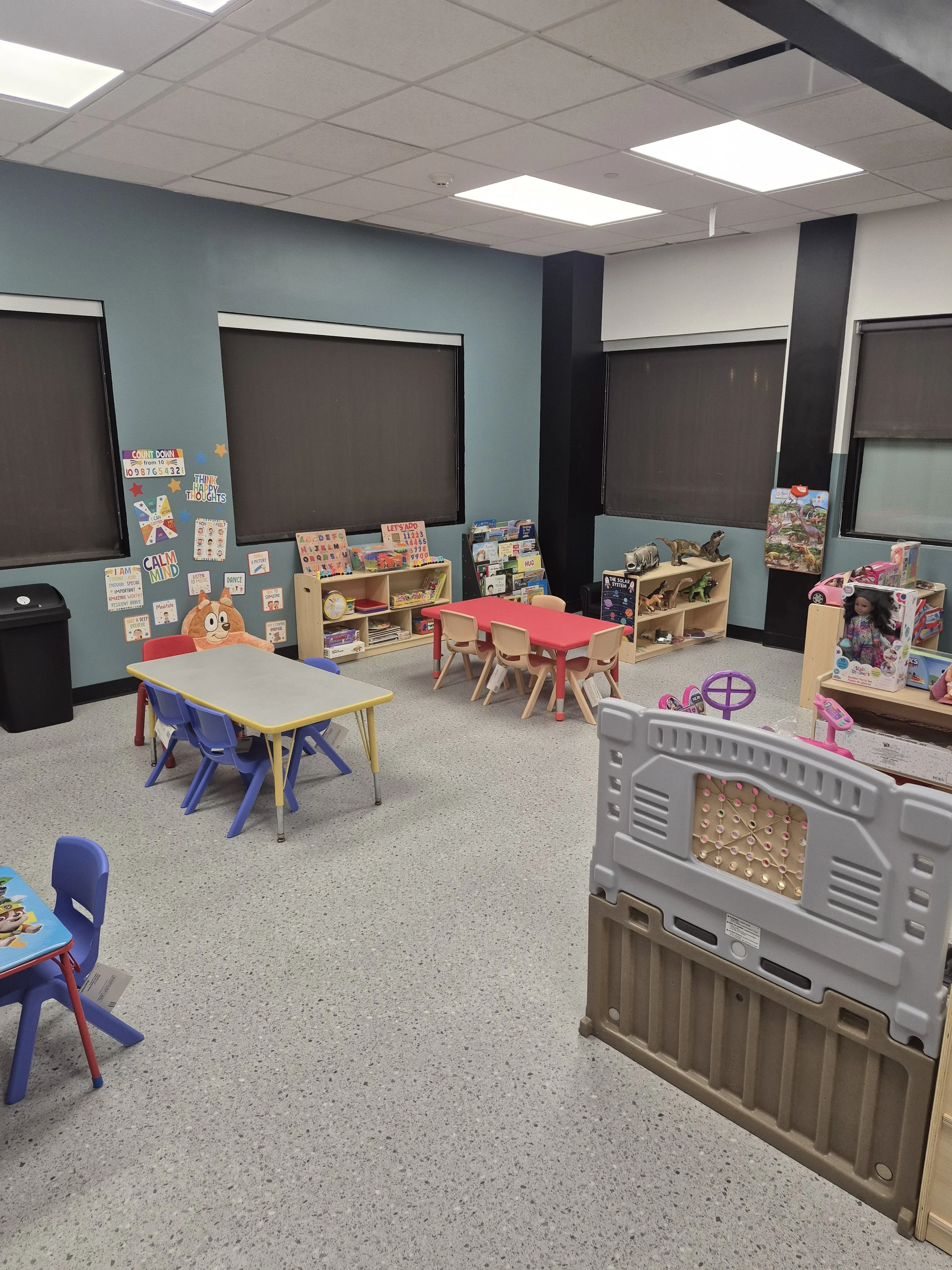 Classroom with child-sized tables, chairs, books, and activity shelves.