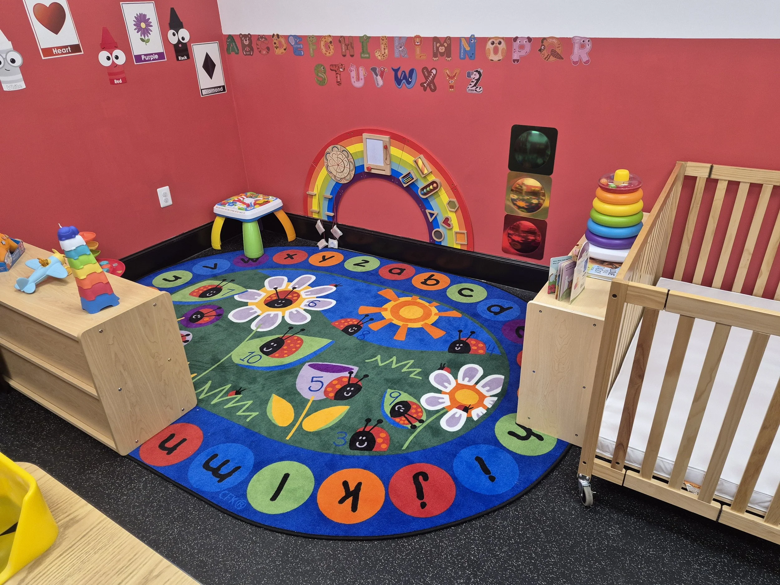 Alphabet play rug surrounded by colorful activity toys and low storage shelves.