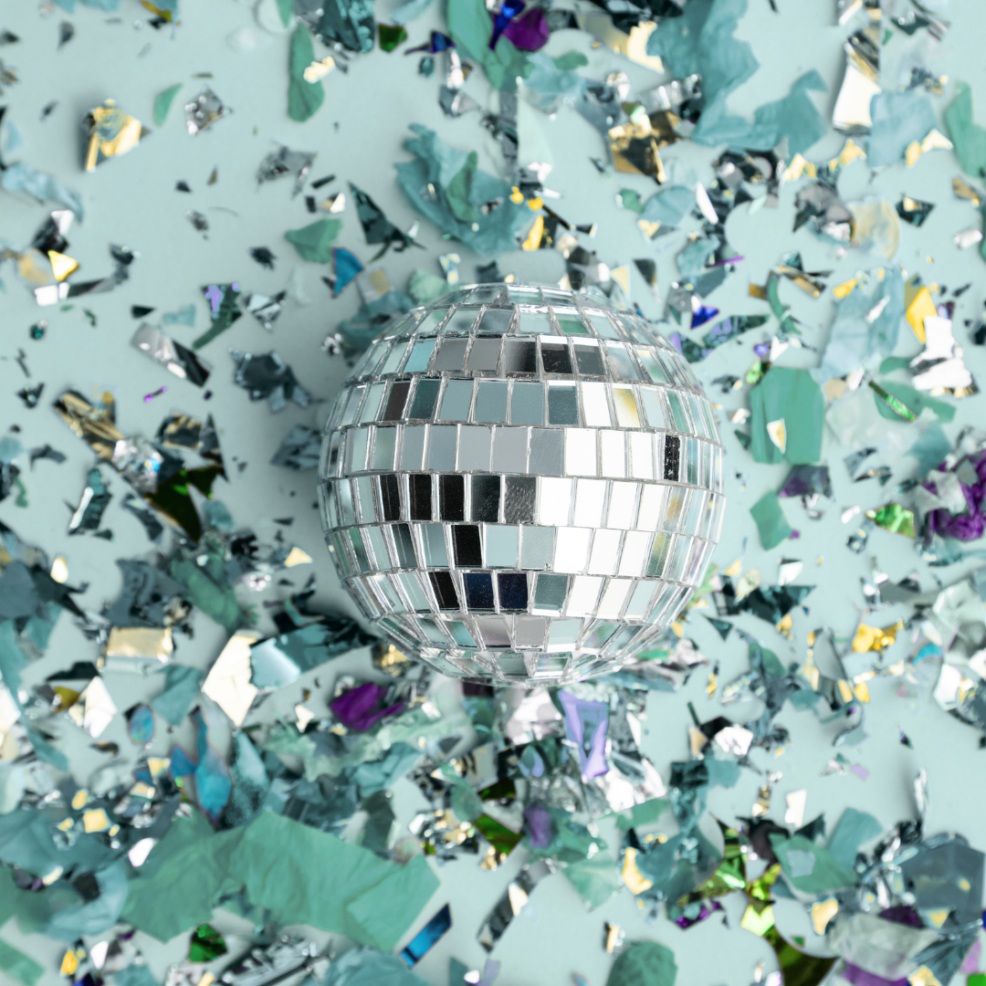 A disco ball surrounded by colorful confetti on a light background.