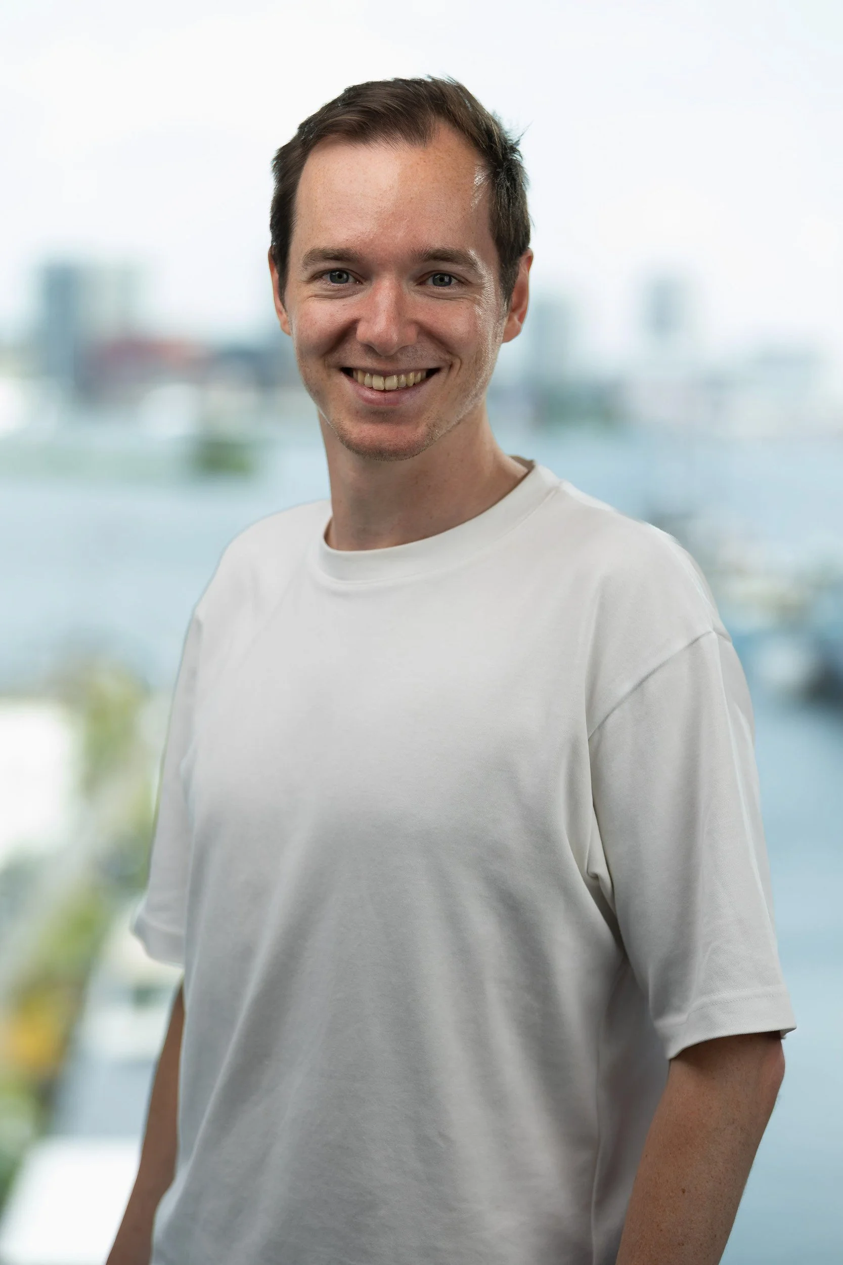 Relaxed male professional headshot in white t-shirt with Amsterdam skyline background — corporate headshot photographer Amsterdam Ballo Studio