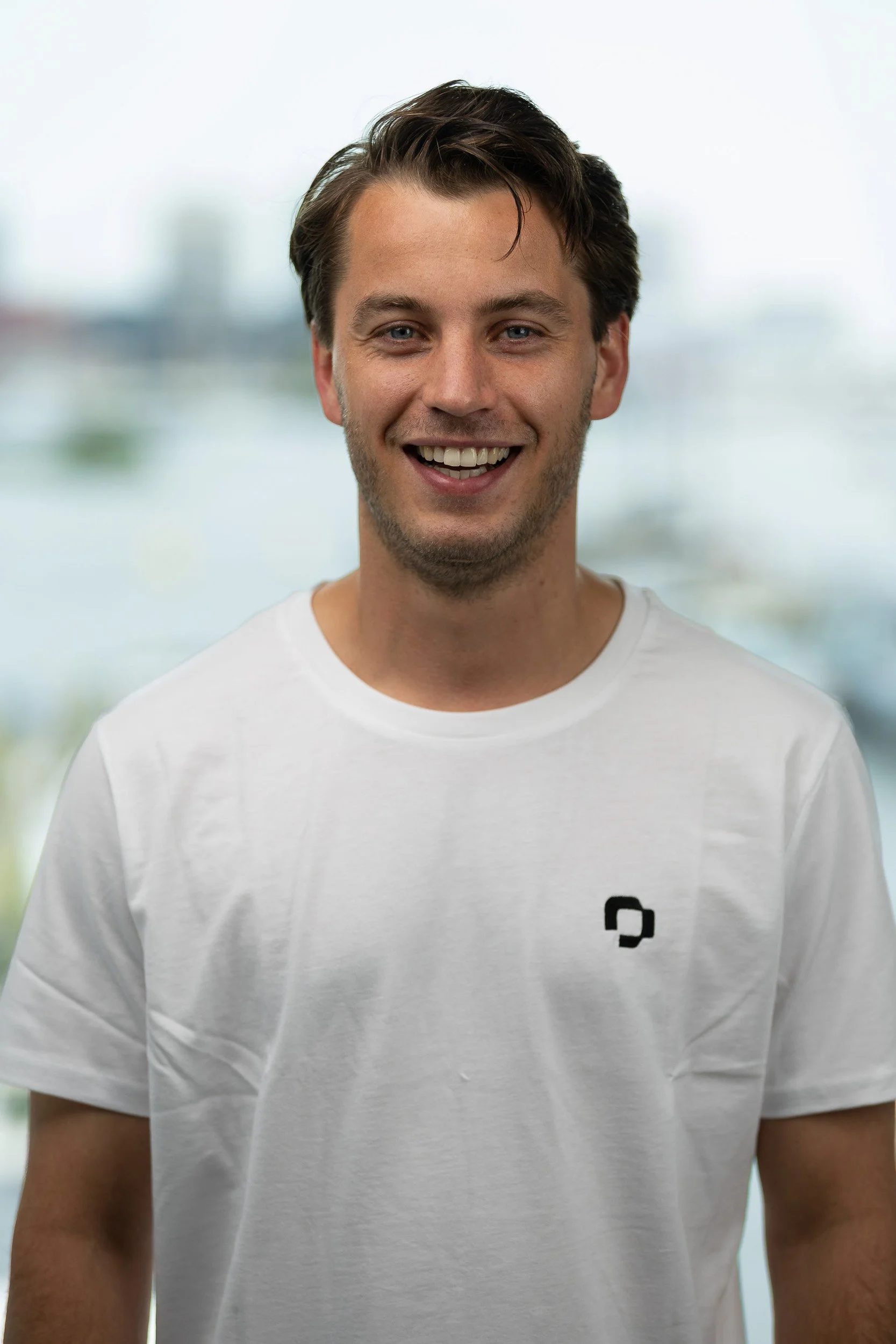 Smiling male employee portrait in white branded t-shirt with Amsterdam background — corporate headshot photographer Amsterdam Ballo Studio