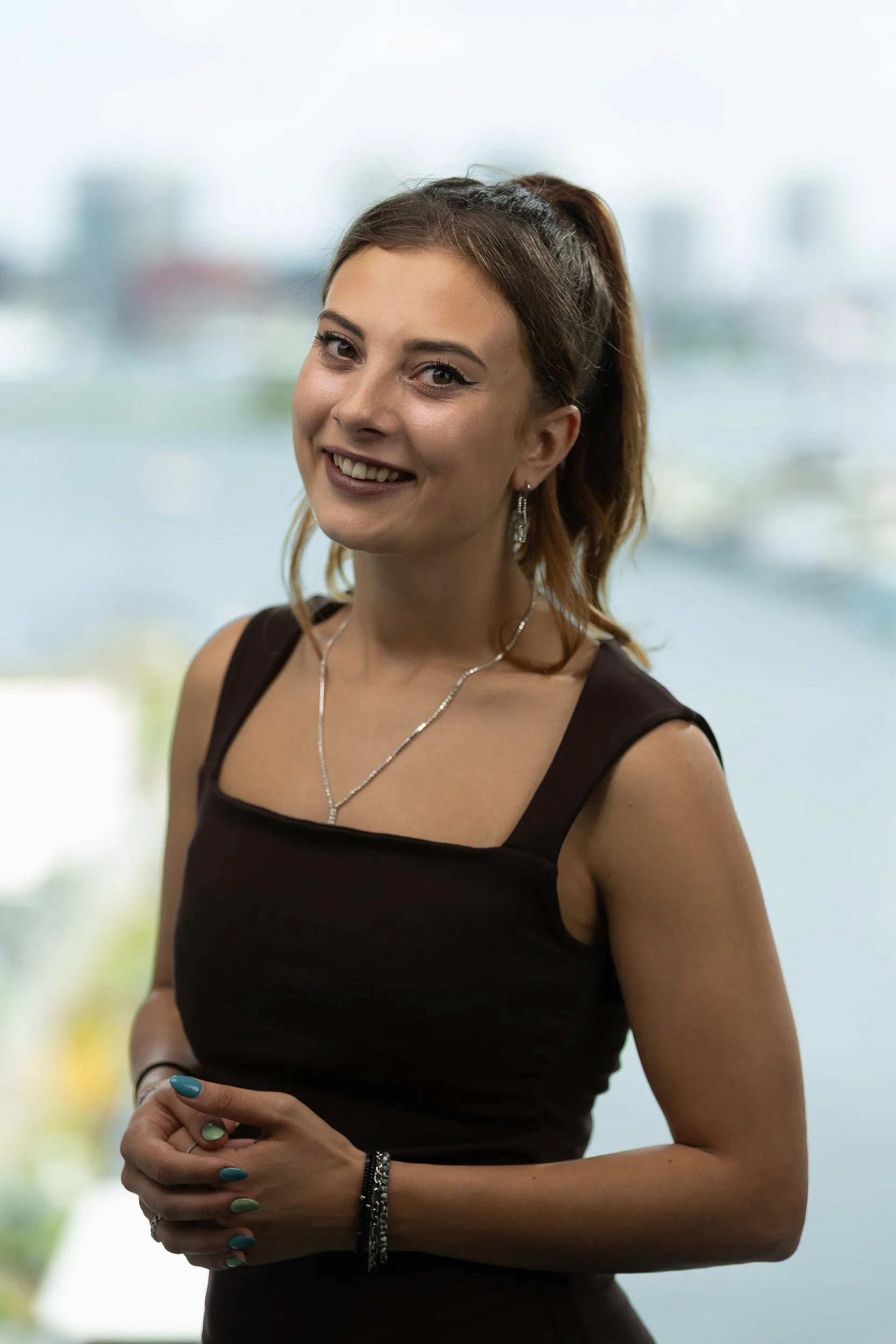 Young professional woman smiling in dark top with Amsterdam waterfront background — corporate headshot photographer Amsterdam Ballo Studio