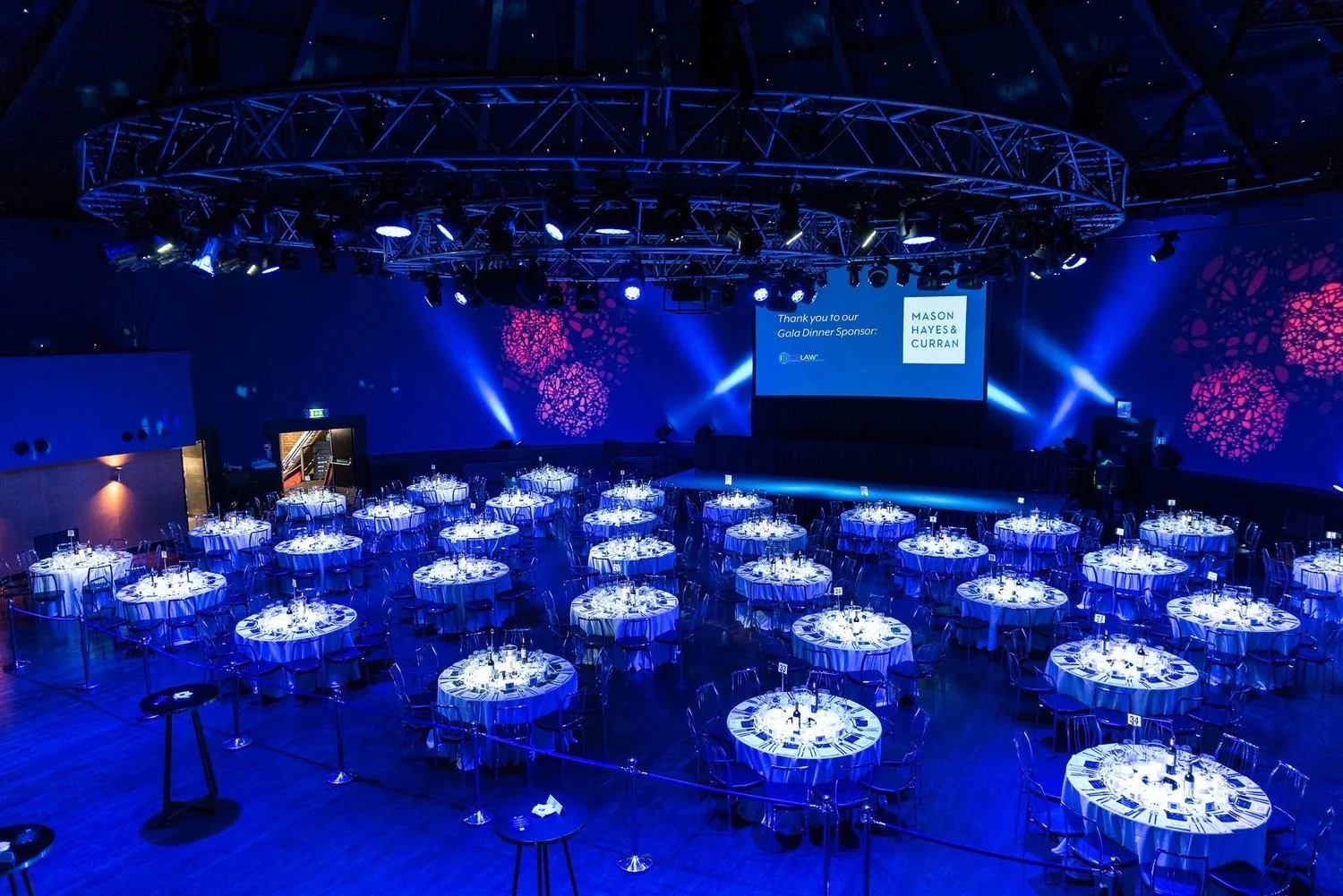 Grand gala dinner venue setup with round tables circular truss lighting and blue stage screens before guests arrive Amsterdam — gala dinner photography Amsterdam Ballo Studio