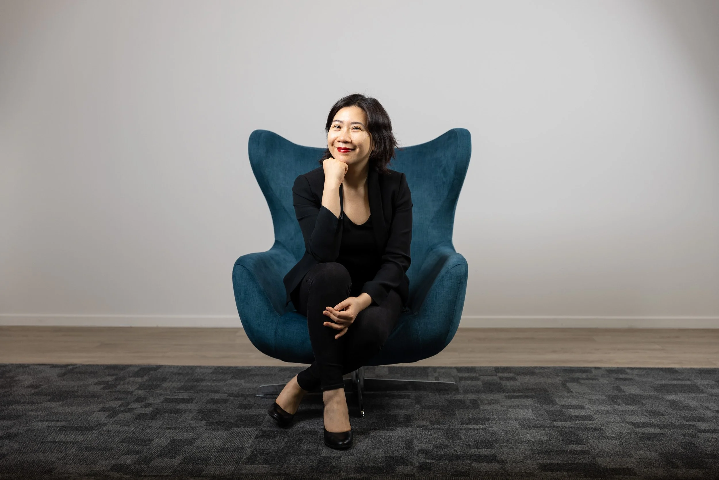 TCI Biotech employee portrait, woman seated in teal egg chair, all black outfit, relaxed editorial pose — corporate headshot photographer Amsterdam Ballo Studio