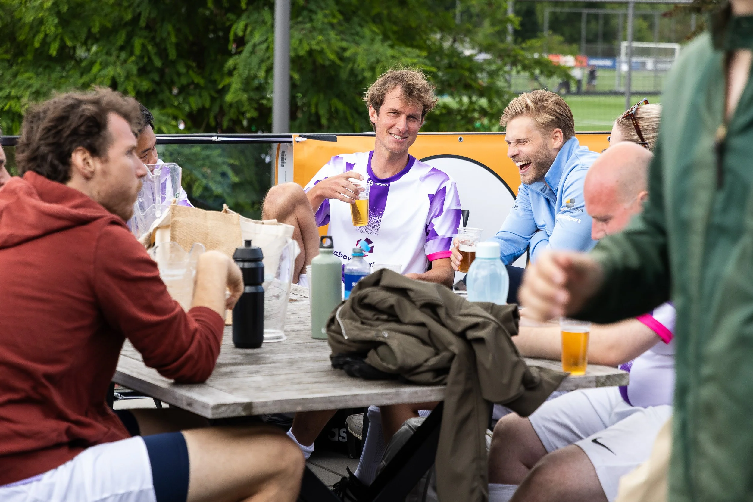 Football players in kit laughing and relaxing with beers between matches at Adfocup 2026 Amsterdam — corporate event photography Amsterdam Ballo Studio