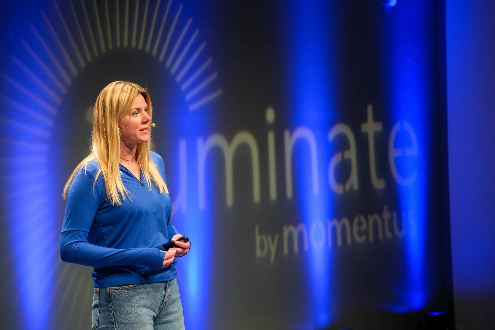 Female keynote speaker on stage in front of Illuminate by Momentus backdrop — Copenhagen event photography Ballo Studio
