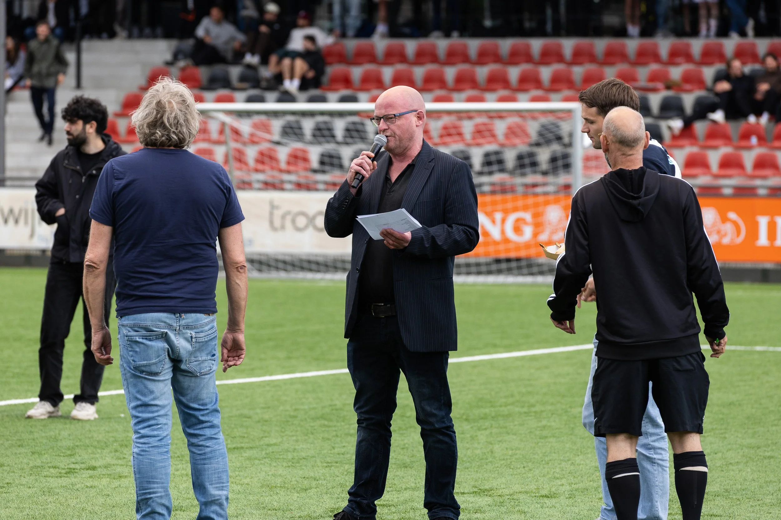MC with microphone addressing participants on pitch at Adfocup 2026 opening ceremony at Amsterdamsche Football Club — event photography Amsterdam Ballo Studio