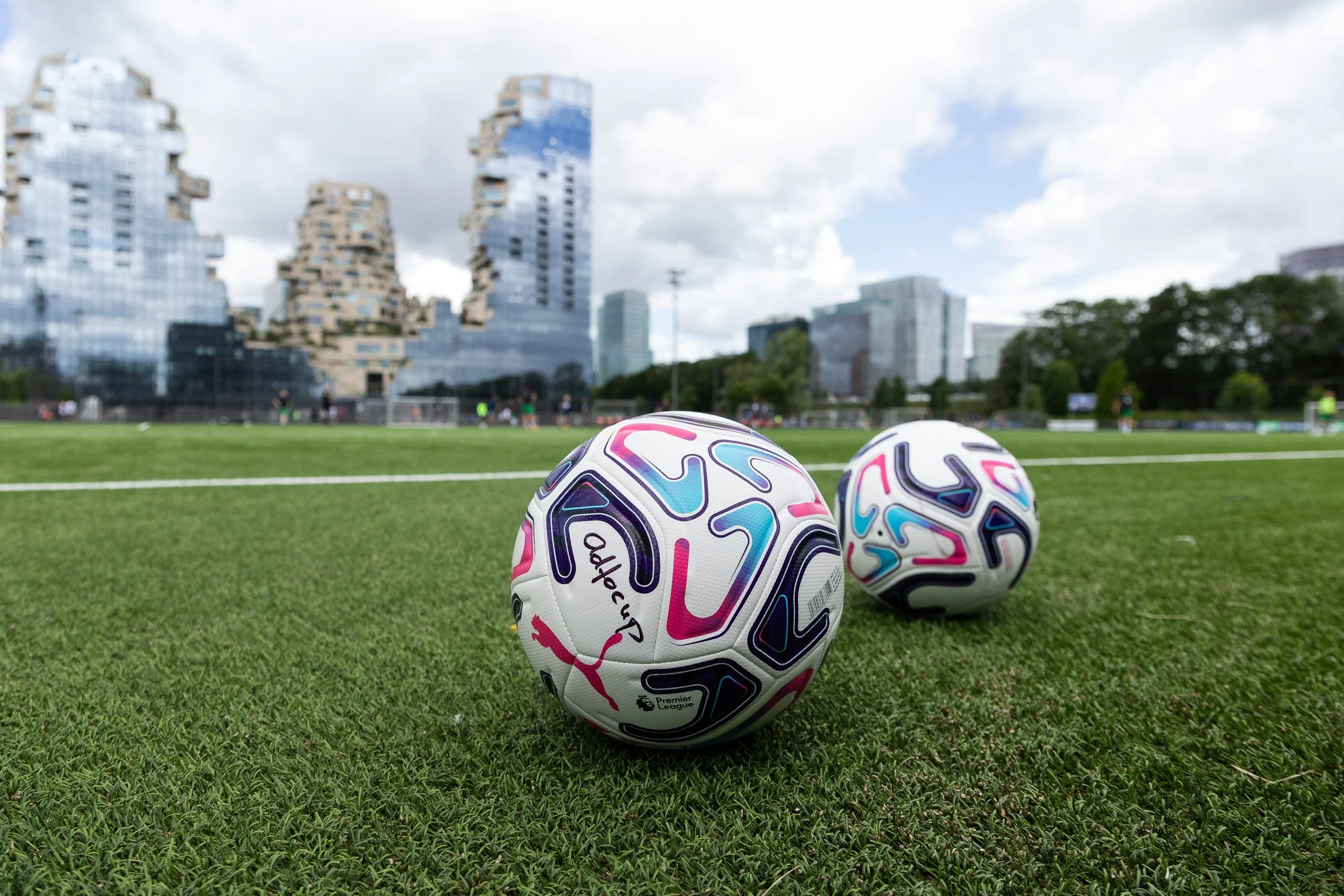 Adfocup branded footballs on pitch with Amsterdam skyline at Adfocup 2026 corporate football tournament — event photography Amsterdam Ballo Studio