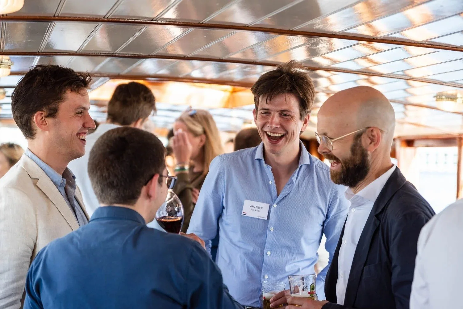 Colleagues laughing and networking aboard Amsterdam canal boat at corporate event reception — corporate event photography Amsterdam Ballo Studio